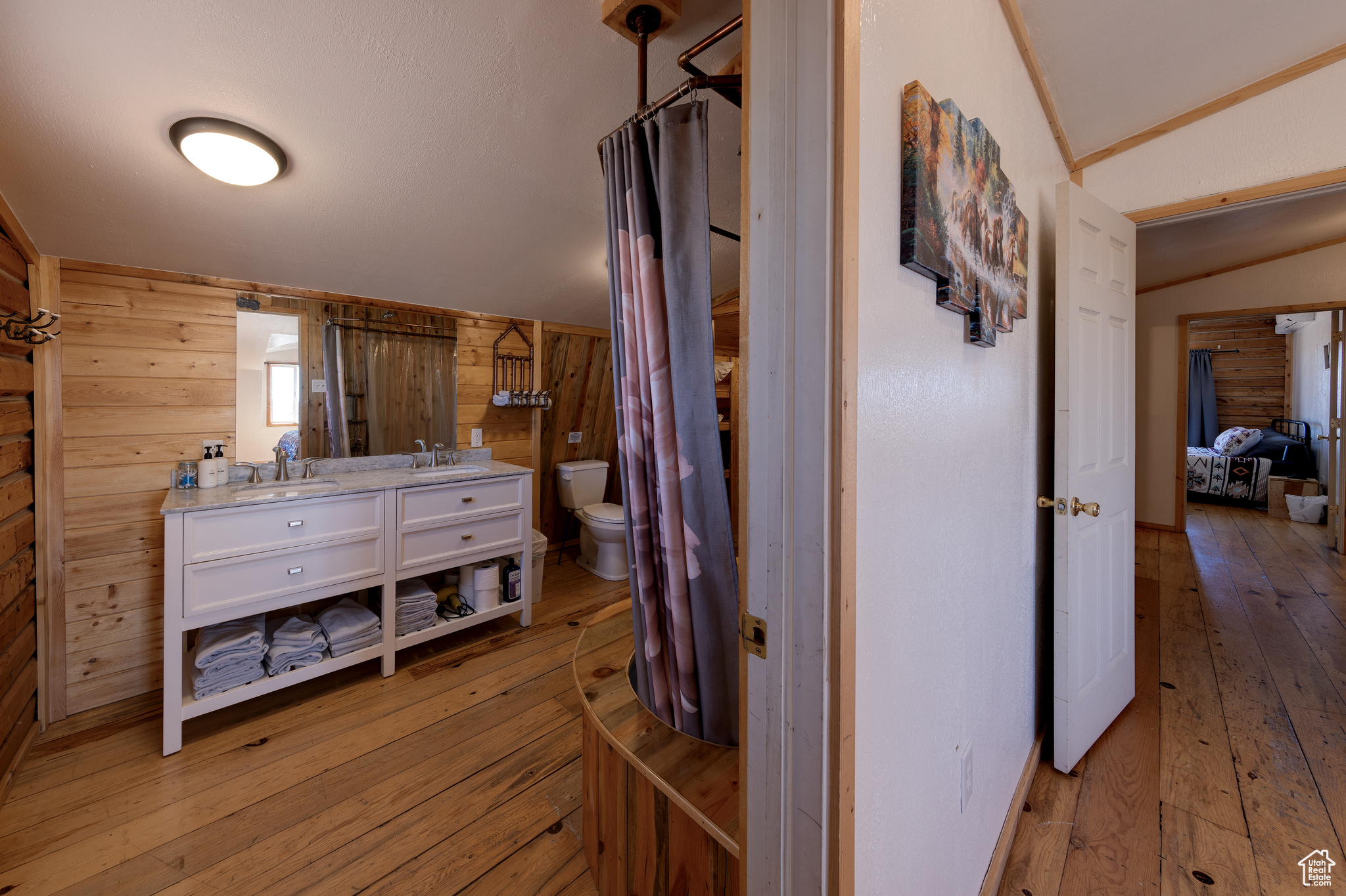 Bathroom with lofted ceiling, toilet, wooden walls, vanity, and hardwood / wood-style flooring