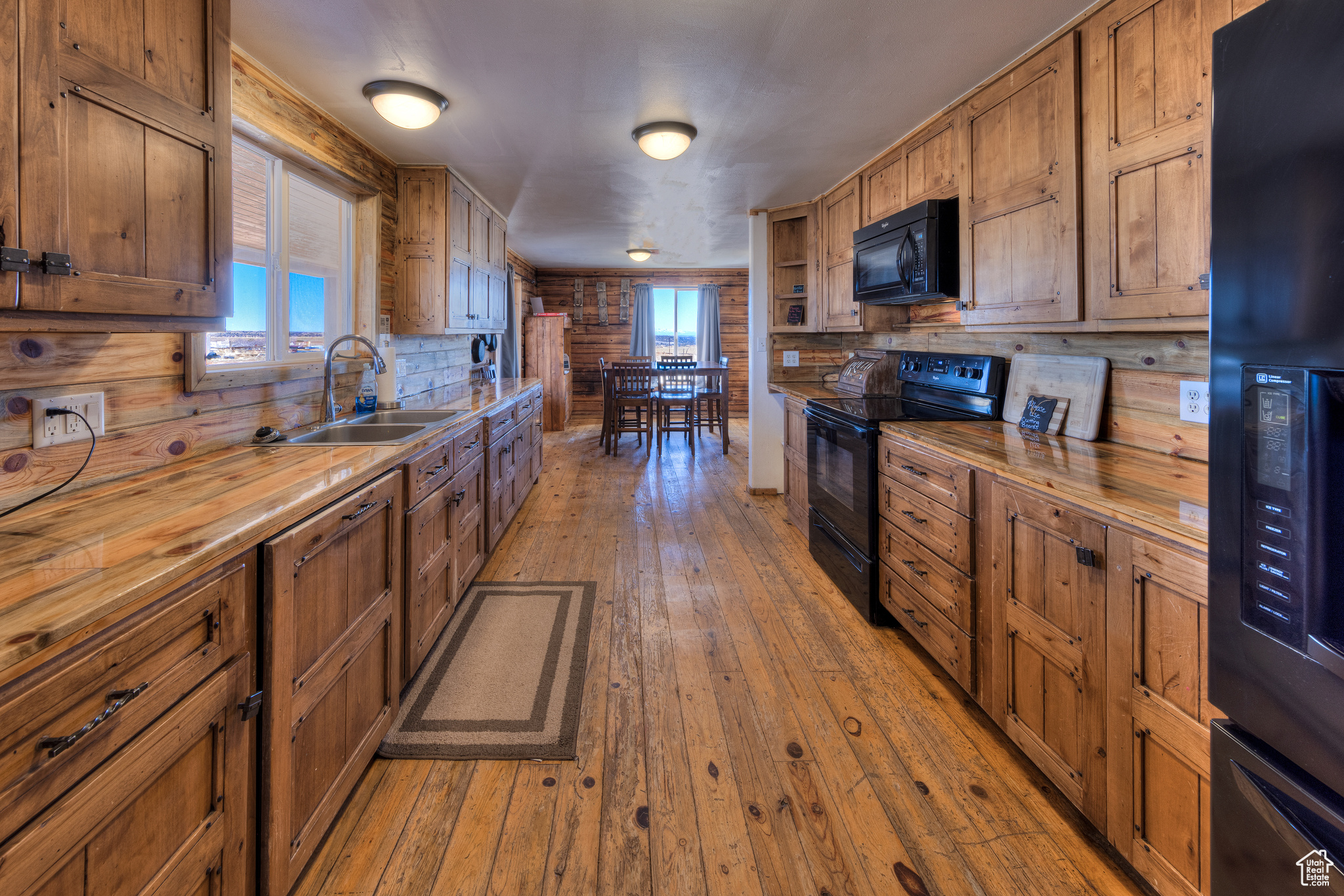 Kitchen with black appliances, wood walls, butcher block counters, and sink