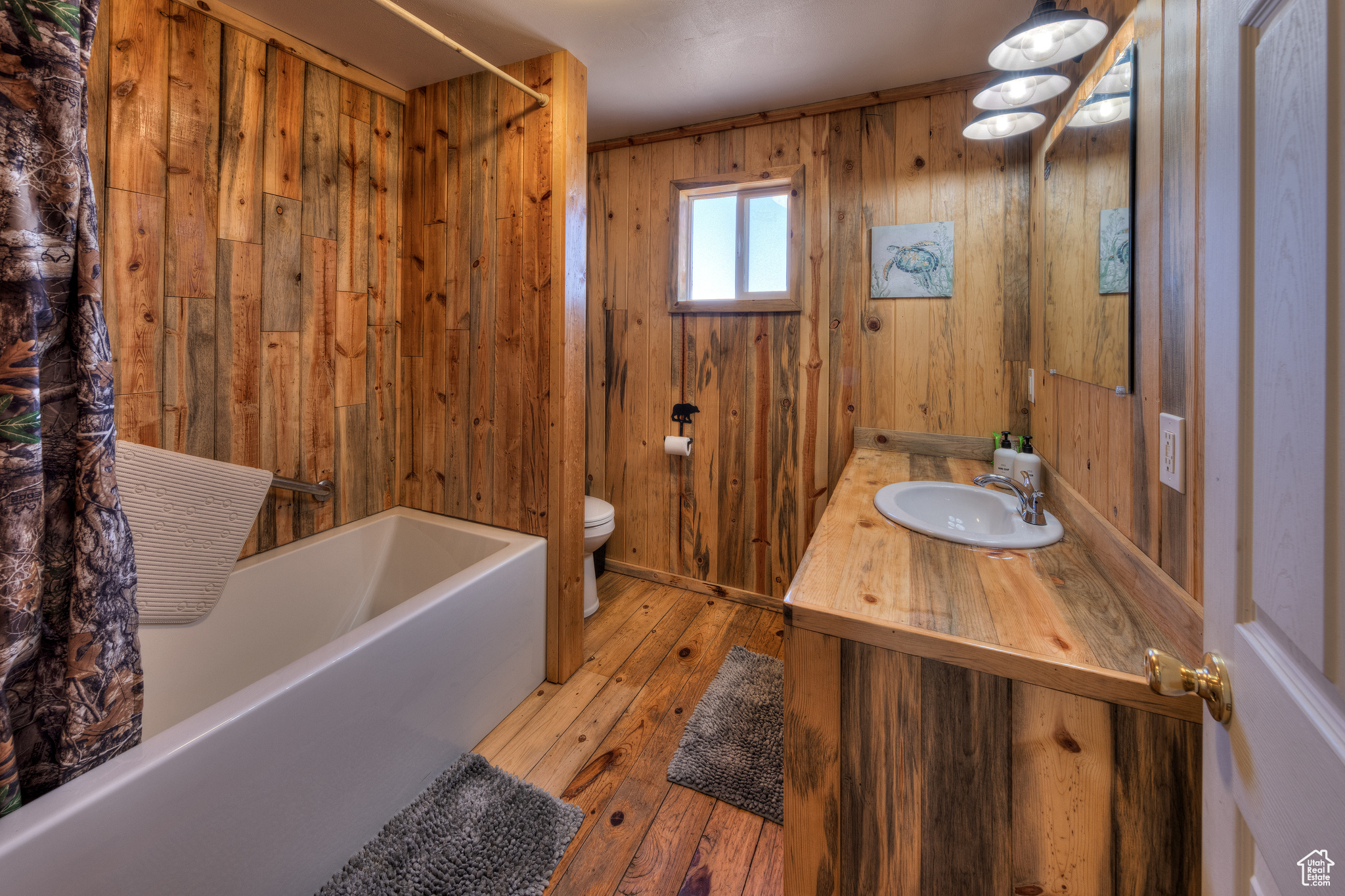 Full bathroom with wood walls, hardwood / wood-style floors, shower / bath combination with curtain, toilet, and vanity