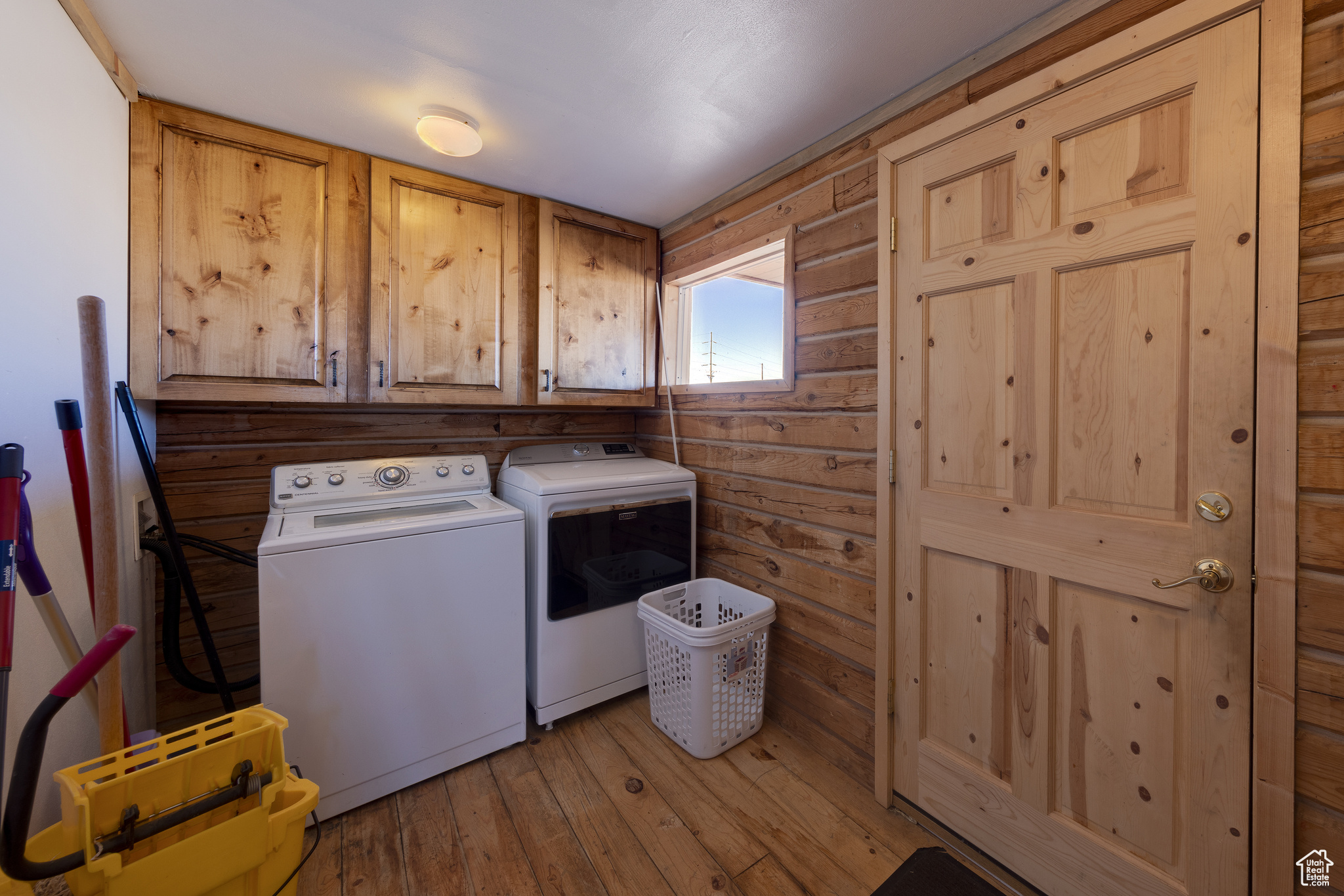 Laundry room featuring cabinets, light wood-type flooring, wooden walls, and washing machine and clothes dryer