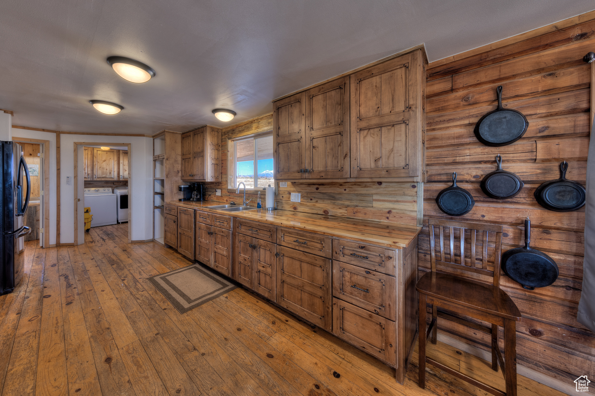 Kitchen with black fridge, sink, light hardwood / wood-style flooring, butcher block countertops, and wood walls