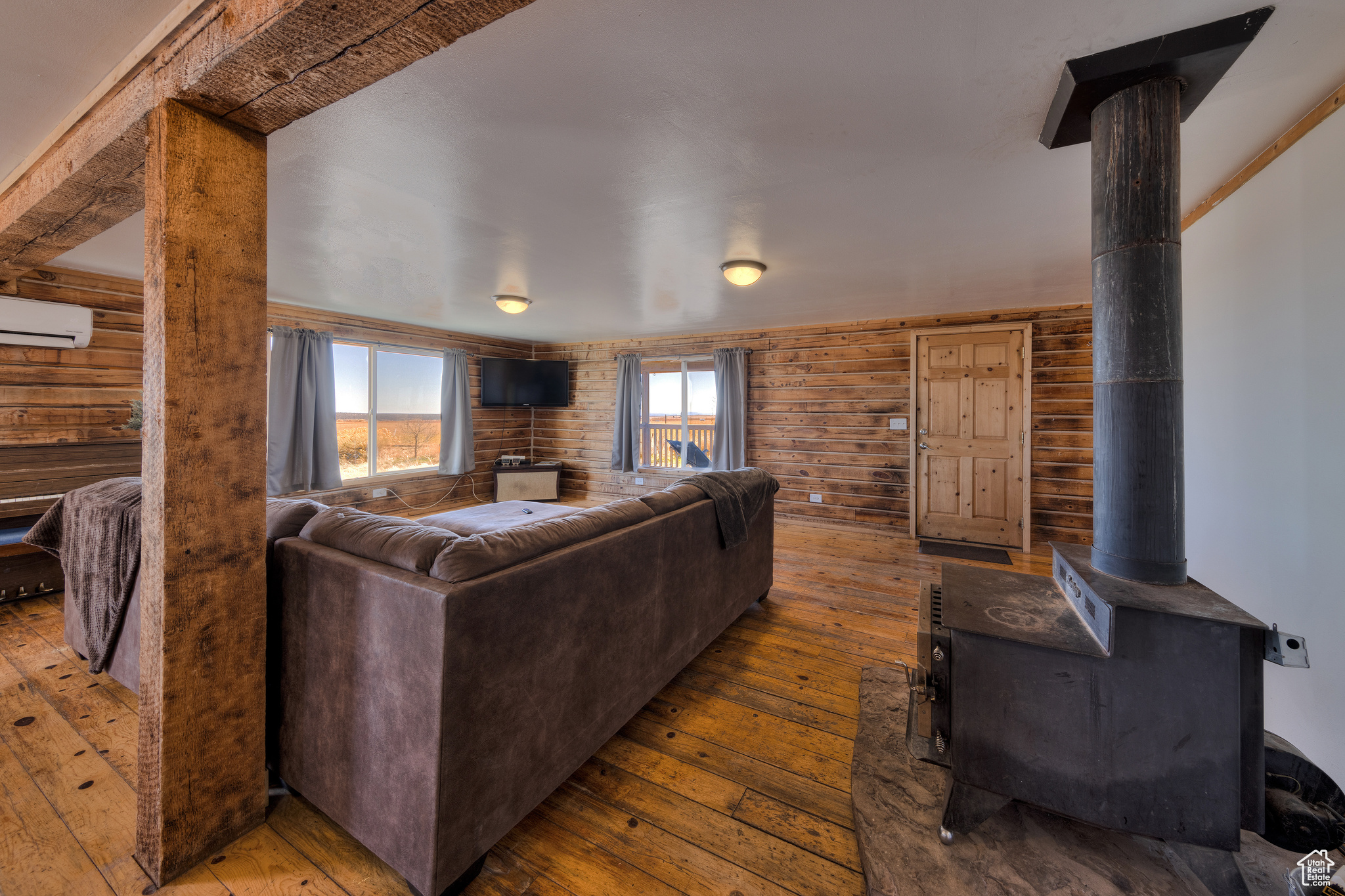 Living room with wood walls, light hardwood / wood-style floors, a wood stove, and a wall unit AC