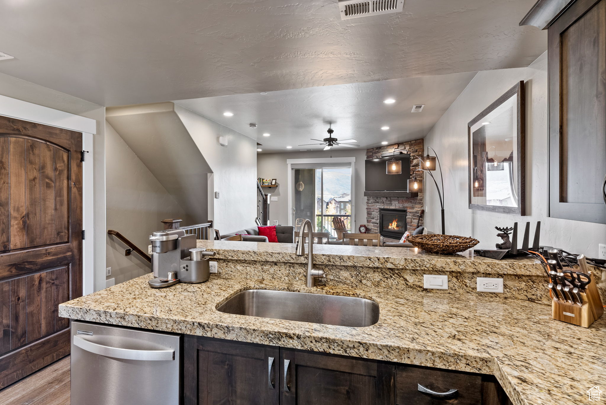 Kitchen featuring light stone countertops, dark brown cabinetry, stainless steel dishwasher, and sink