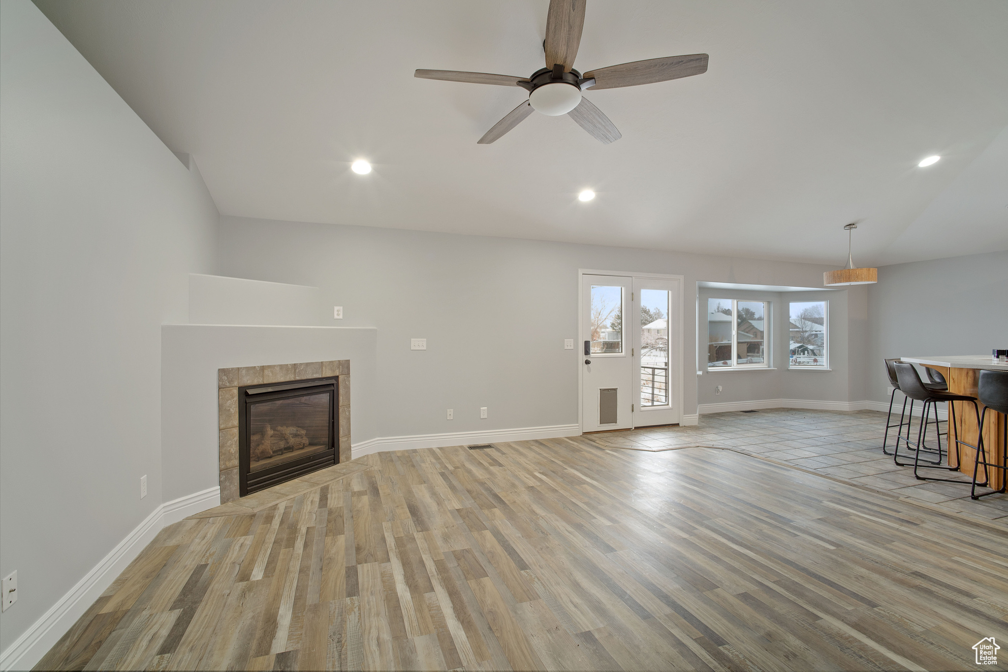 Unfurnished living room with a tiled fireplace, ceiling fan, light hardwood / wood-style floors, and vaulted ceiling