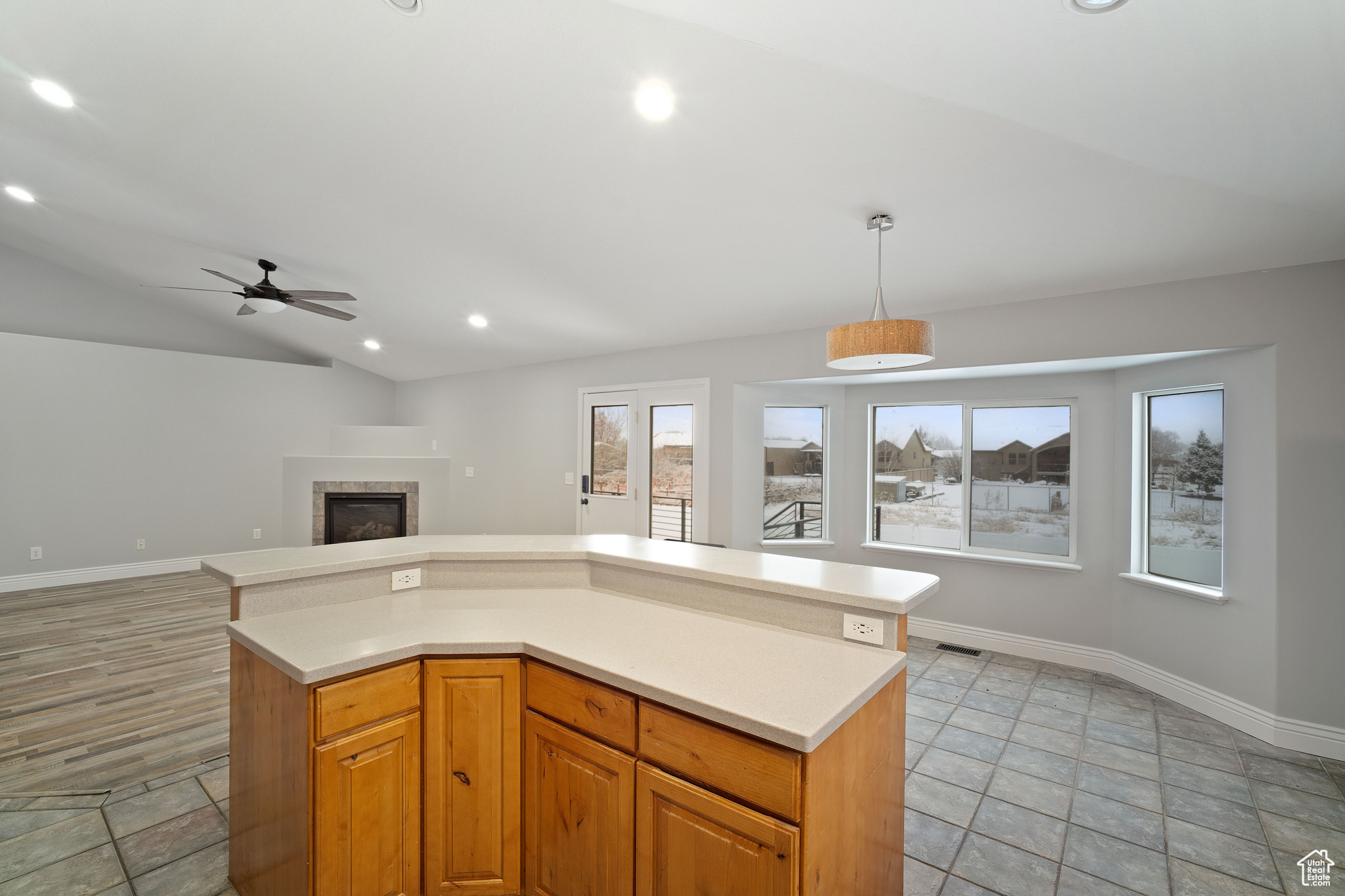 Kitchen featuring a center island, lofted ceiling, ceiling fan, decorative light fixtures, and a tiled fireplace