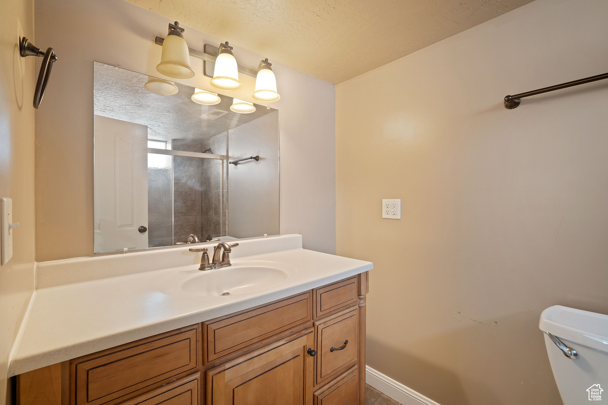 Bathroom with an enclosed shower, vanity, toilet, and a textured ceiling