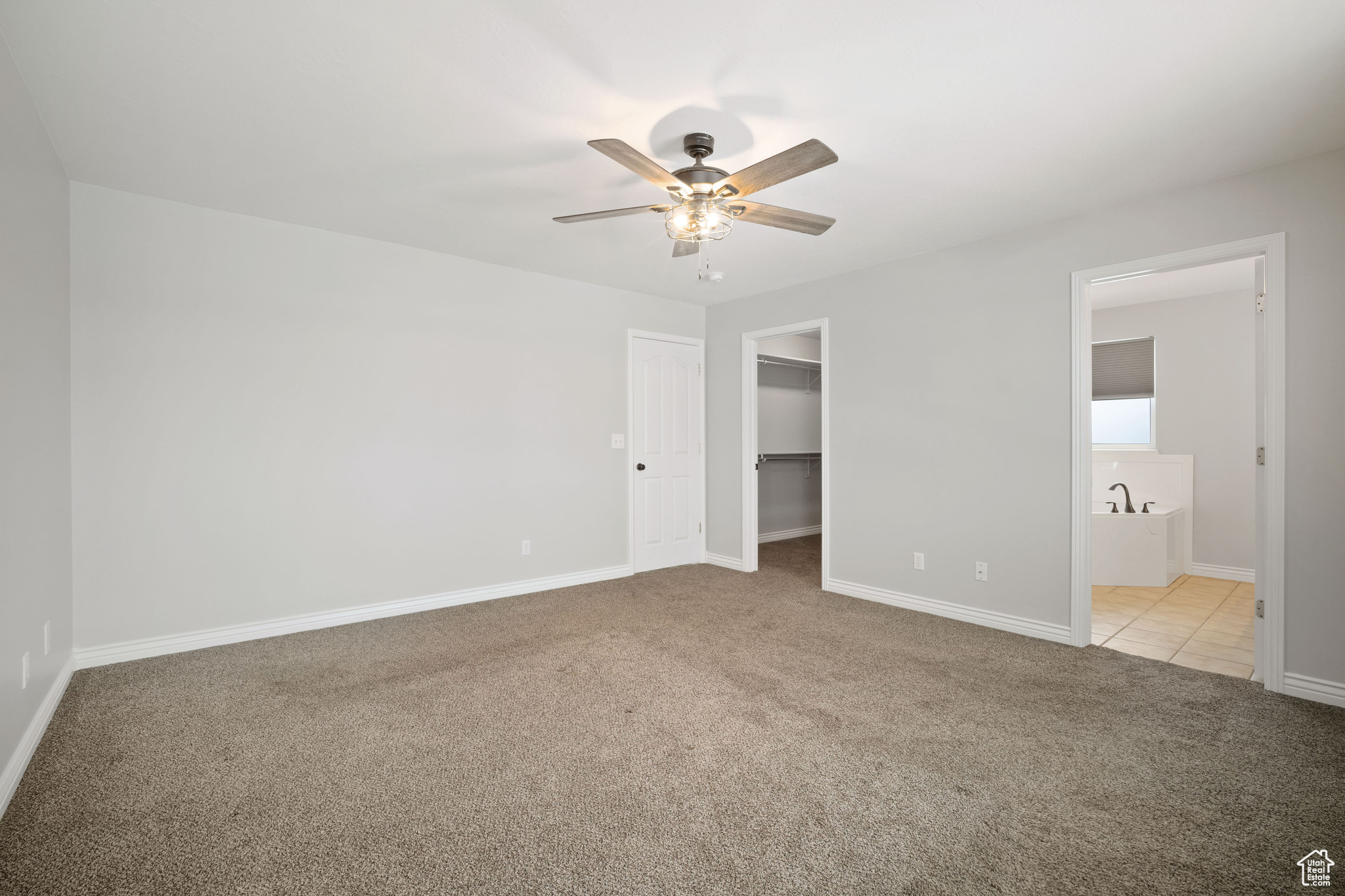 Unfurnished bedroom with ceiling fan, light colored carpet, a spacious closet, and ensuite bath