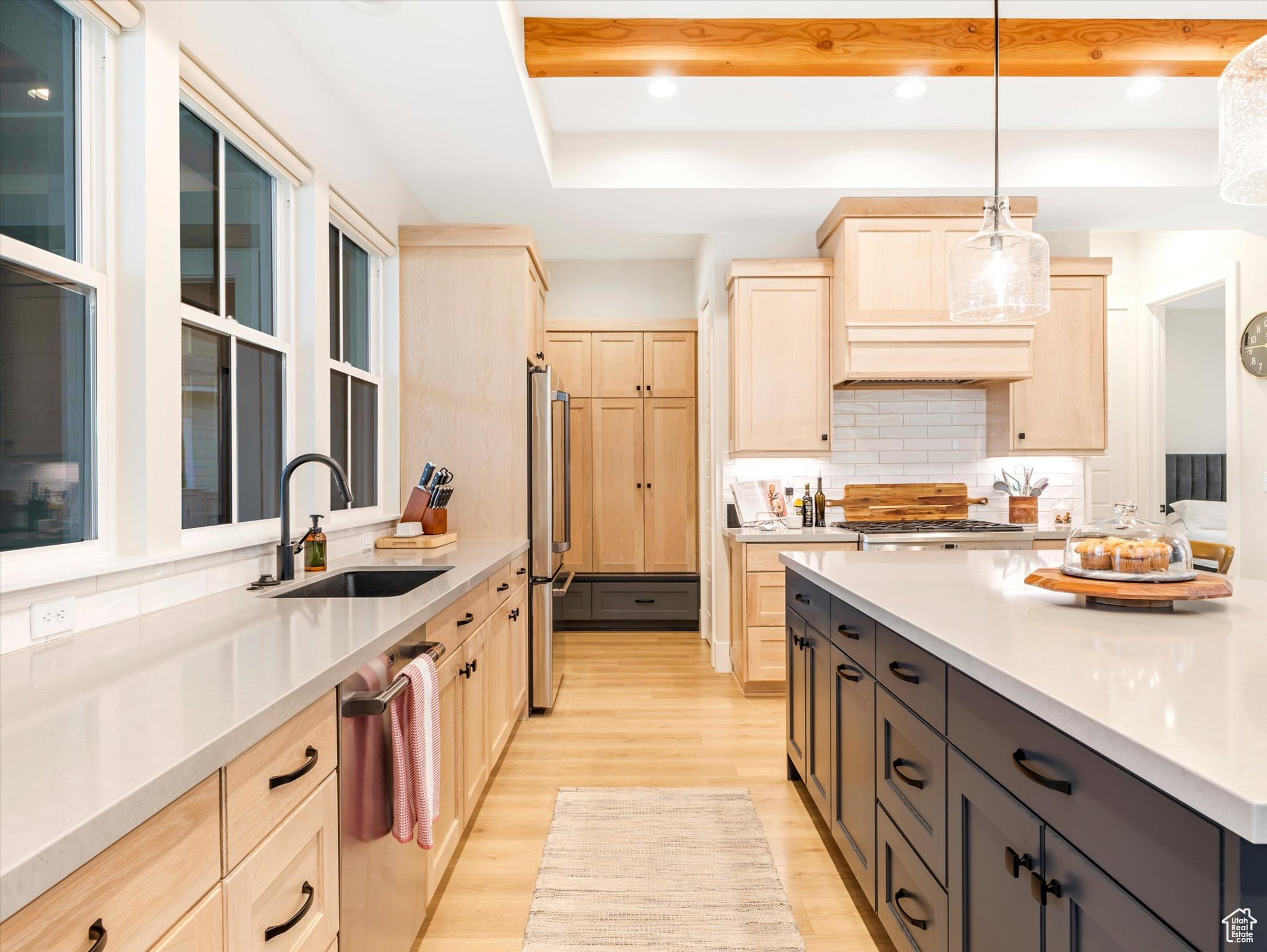 Kitchen featuring light brown cabinets, sink, appliances with stainless steel finishes, decorative light fixtures, and light hardwood / wood-style floors