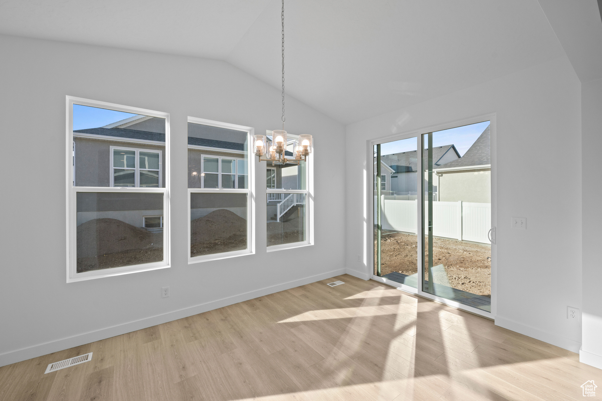 Unfurnished dining area featuring light wood-type flooring, vaulted ceiling, and a notable chandelier