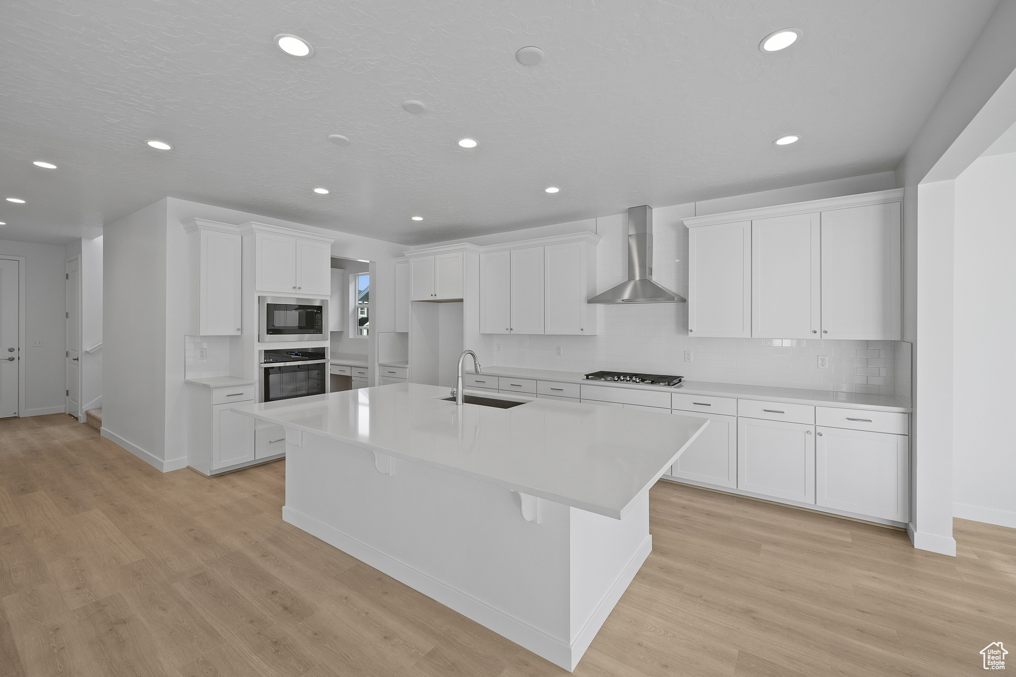 Kitchen with white cabinetry, sink, wall chimney range hood, a center island with sink, and appliances with stainless steel finishes