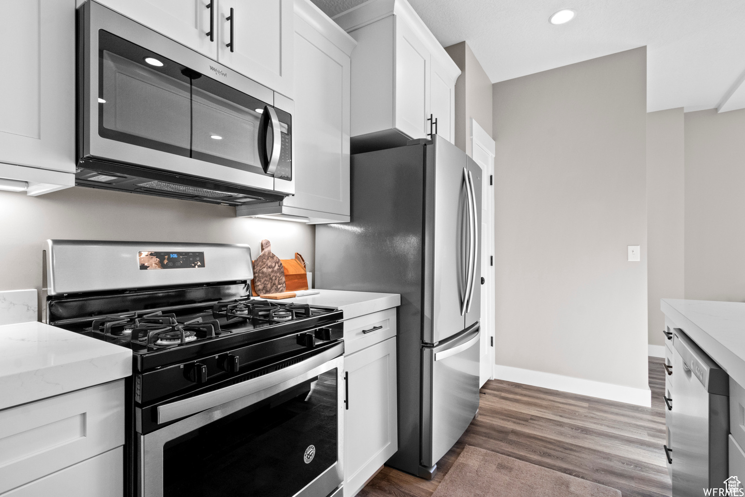 Kitchen featuring light stone countertops, appliances with stainless steel finishes, dark hardwood / wood-style flooring, and white cabinetry