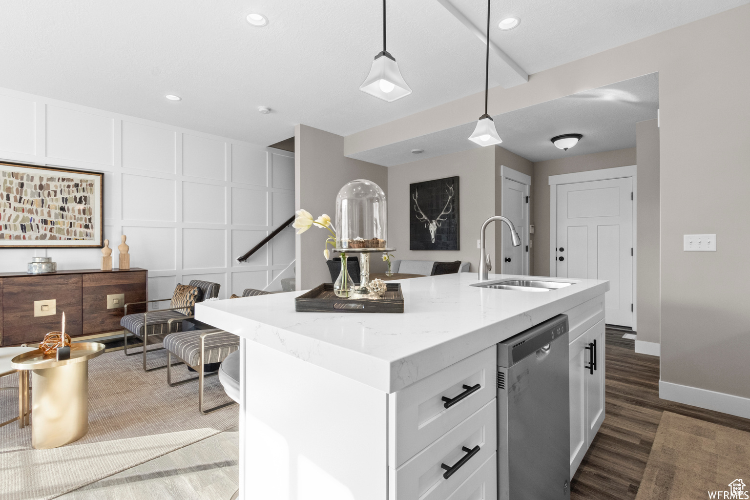 Kitchen with stainless steel dishwasher, a kitchen island with sink, sink, white cabinets, and hanging light fixtures