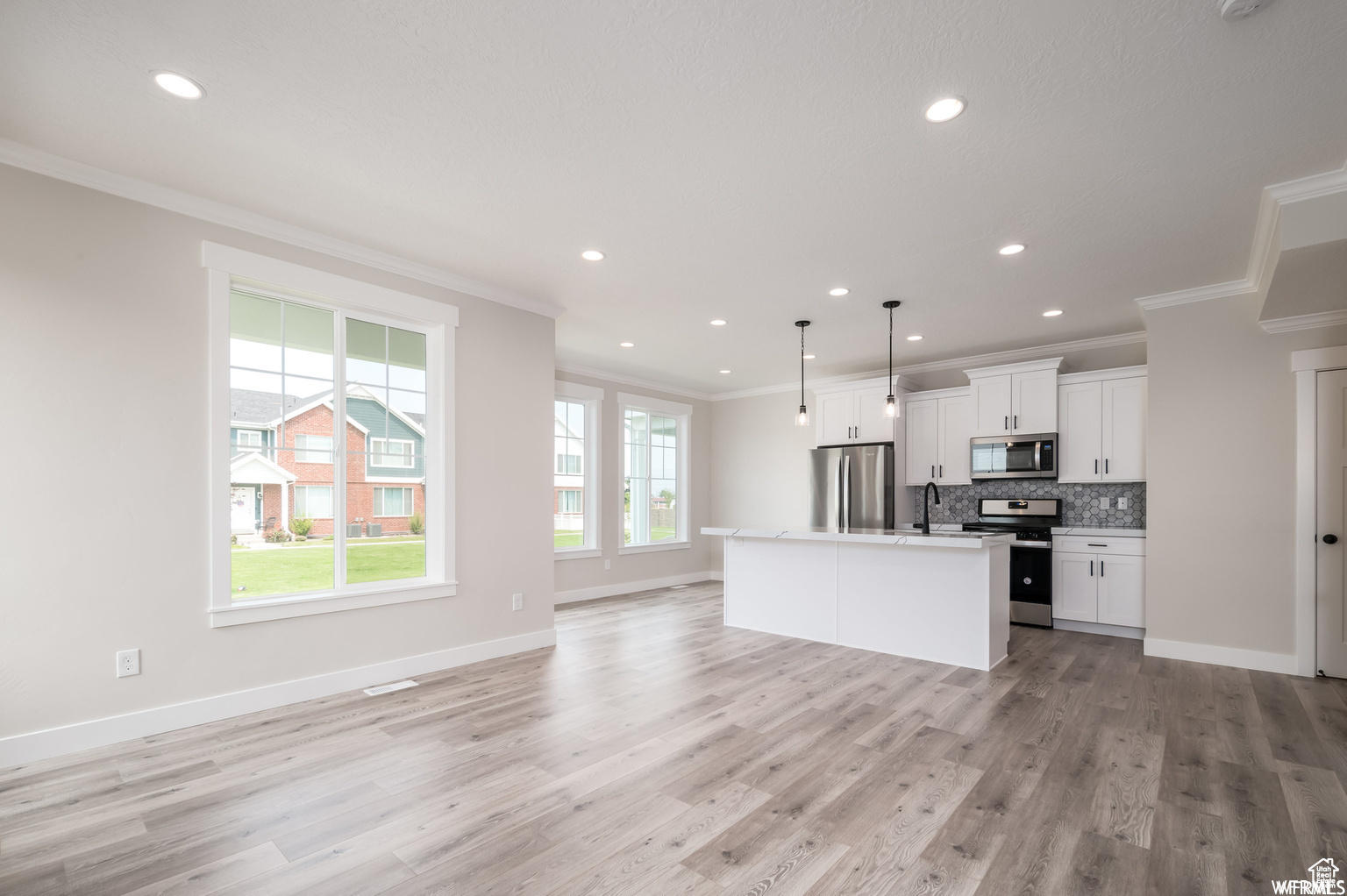 Kitchen with decorative backsplash, appliances with stainless steel finishes, a center island, white cabinetry, and hanging light fixtures