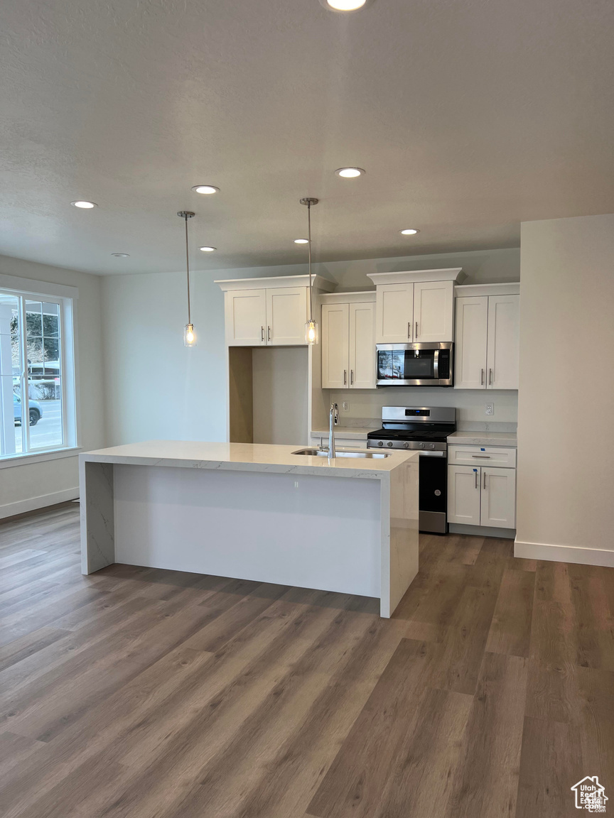 Kitchen with appliances with stainless steel finishes, a kitchen island with sink, decorative light fixtures, white cabinets, and dark hardwood / wood-style floors