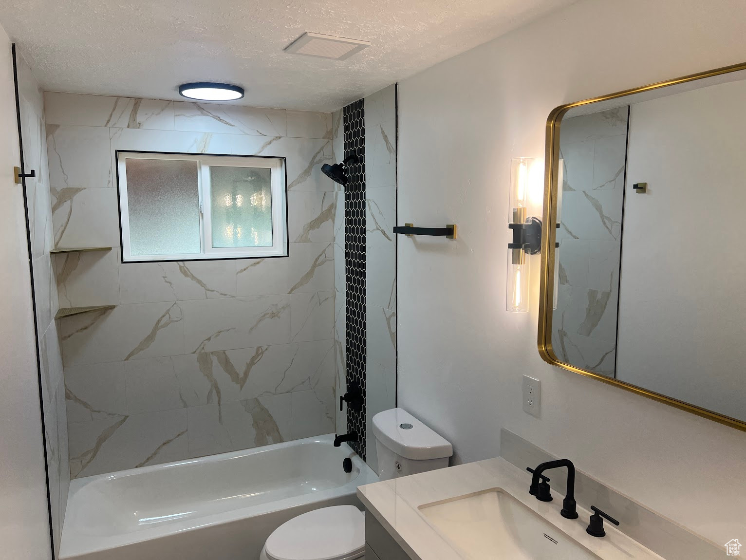 Full bathroom featuring vanity, a textured ceiling, tiled shower / bath combo, and toilet