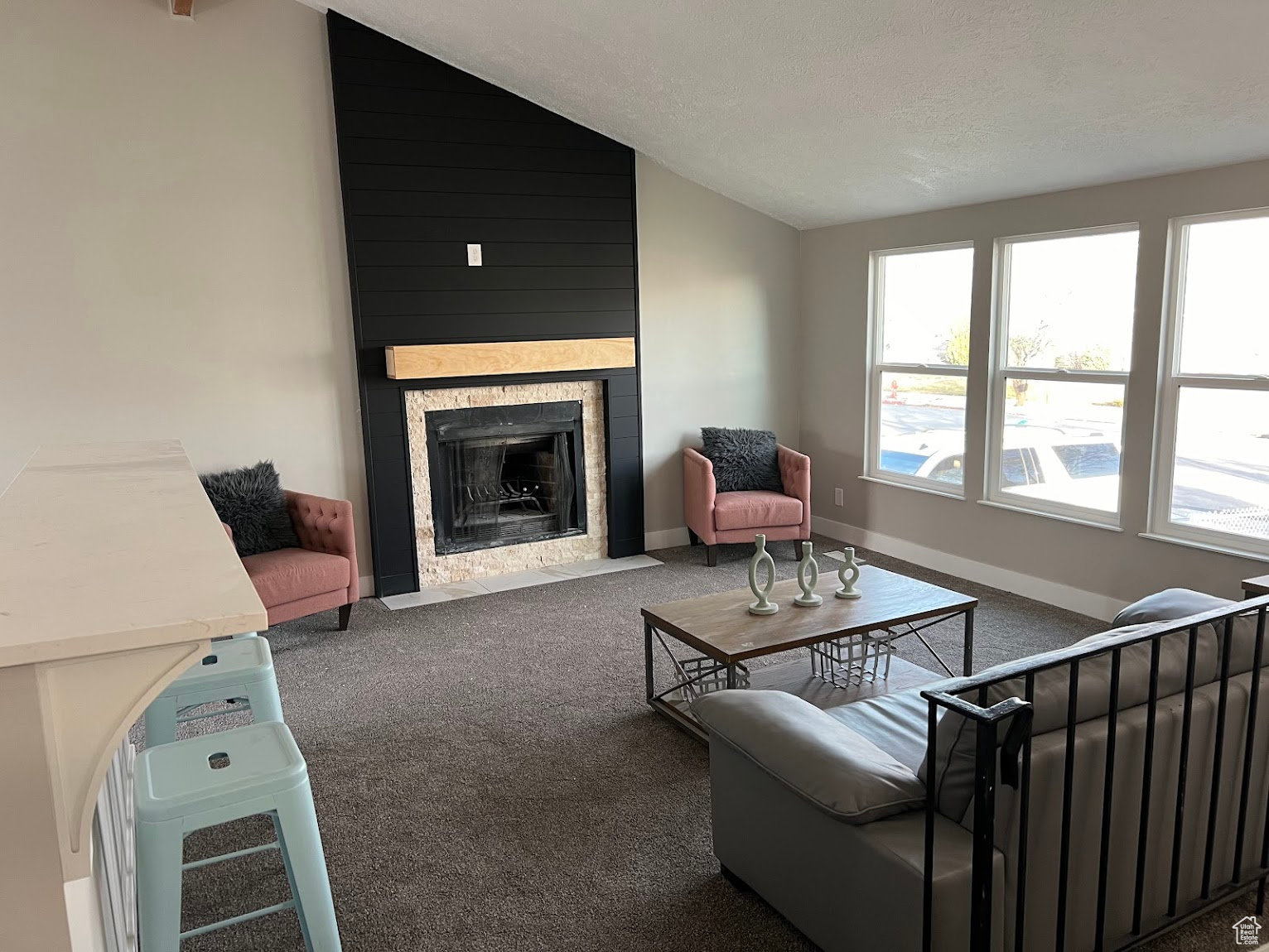 Carpeted living room with a large fireplace, vaulted ceiling, and plenty of natural light