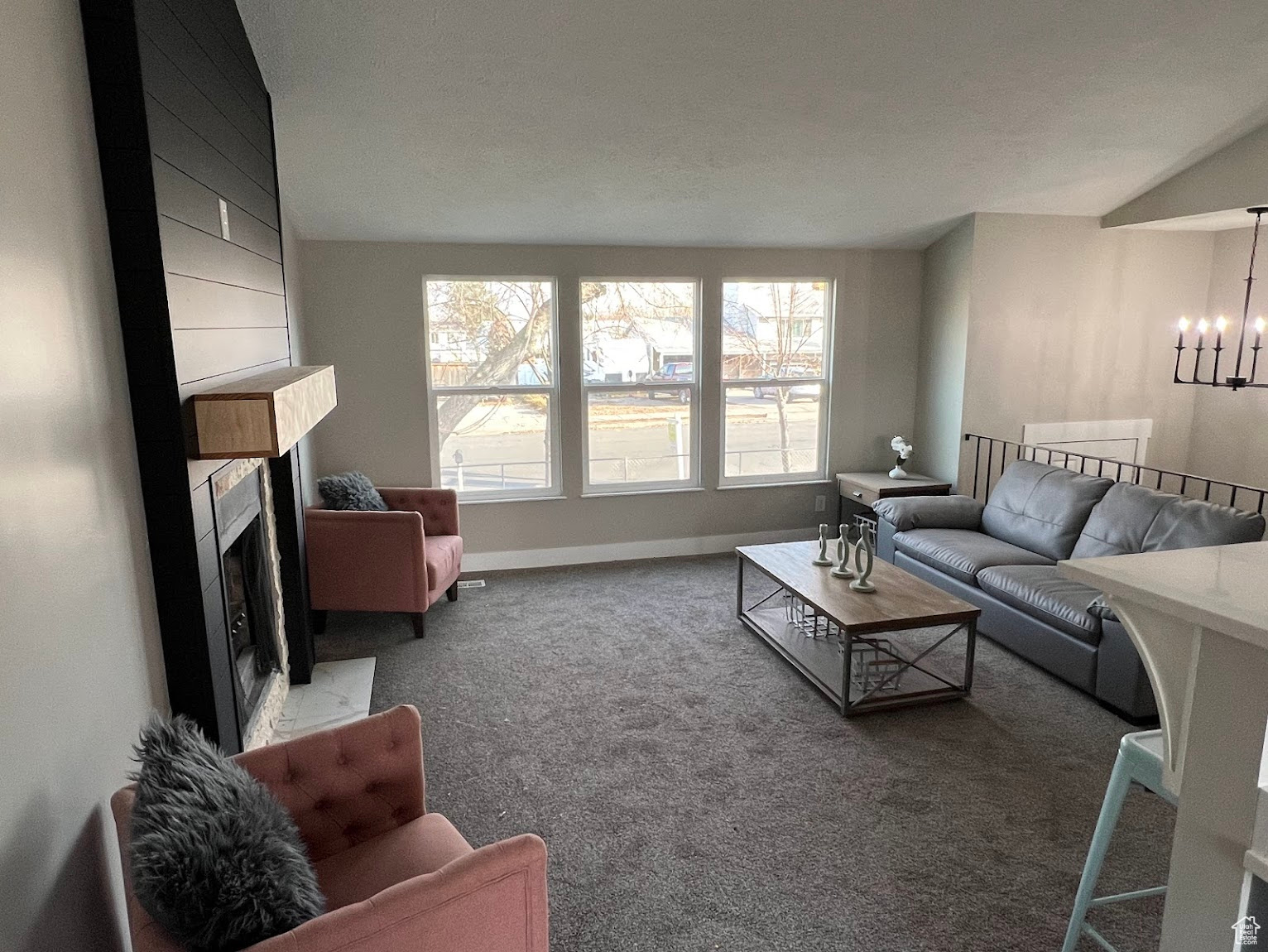 Carpeted living room featuring a notable chandelier, plenty of natural light, a large fireplace, and lofted ceiling