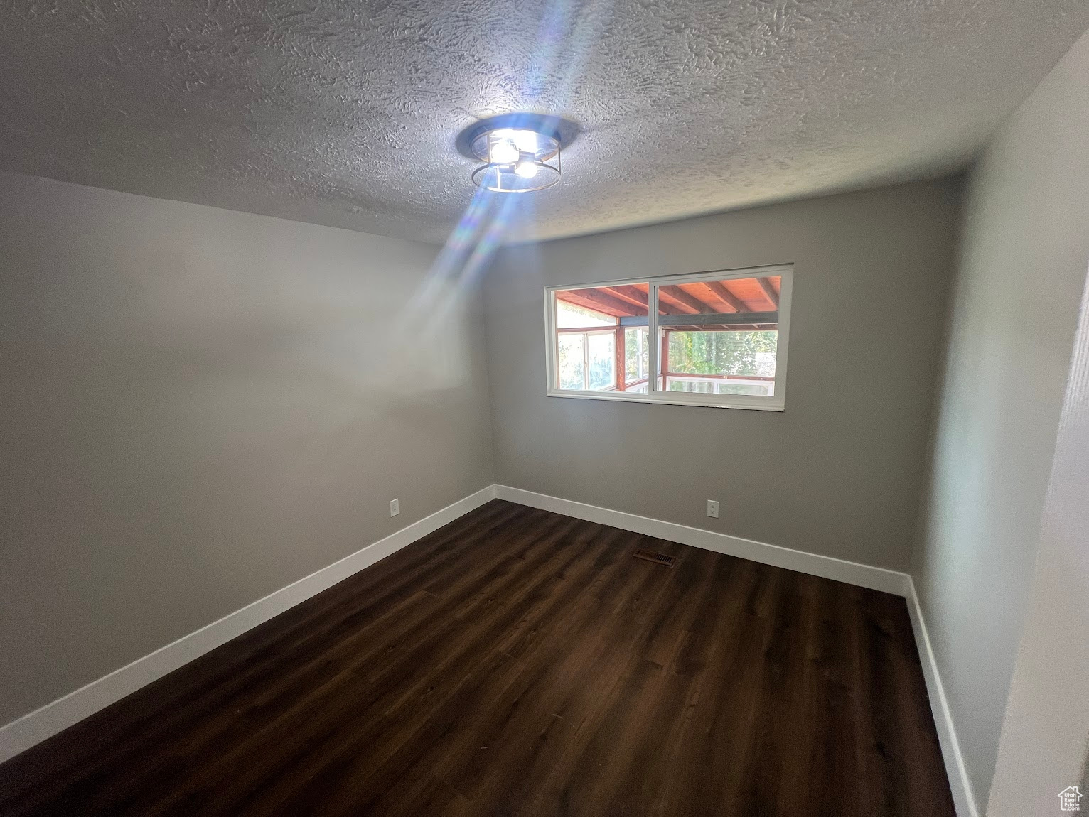 Unfurnished room featuring dark hardwood / wood-style flooring and a textured ceiling