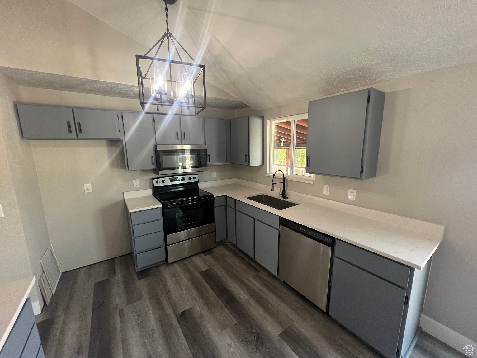 Kitchen with appliances with stainless steel finishes, vaulted ceiling, sink, pendant lighting, and gray cabinets