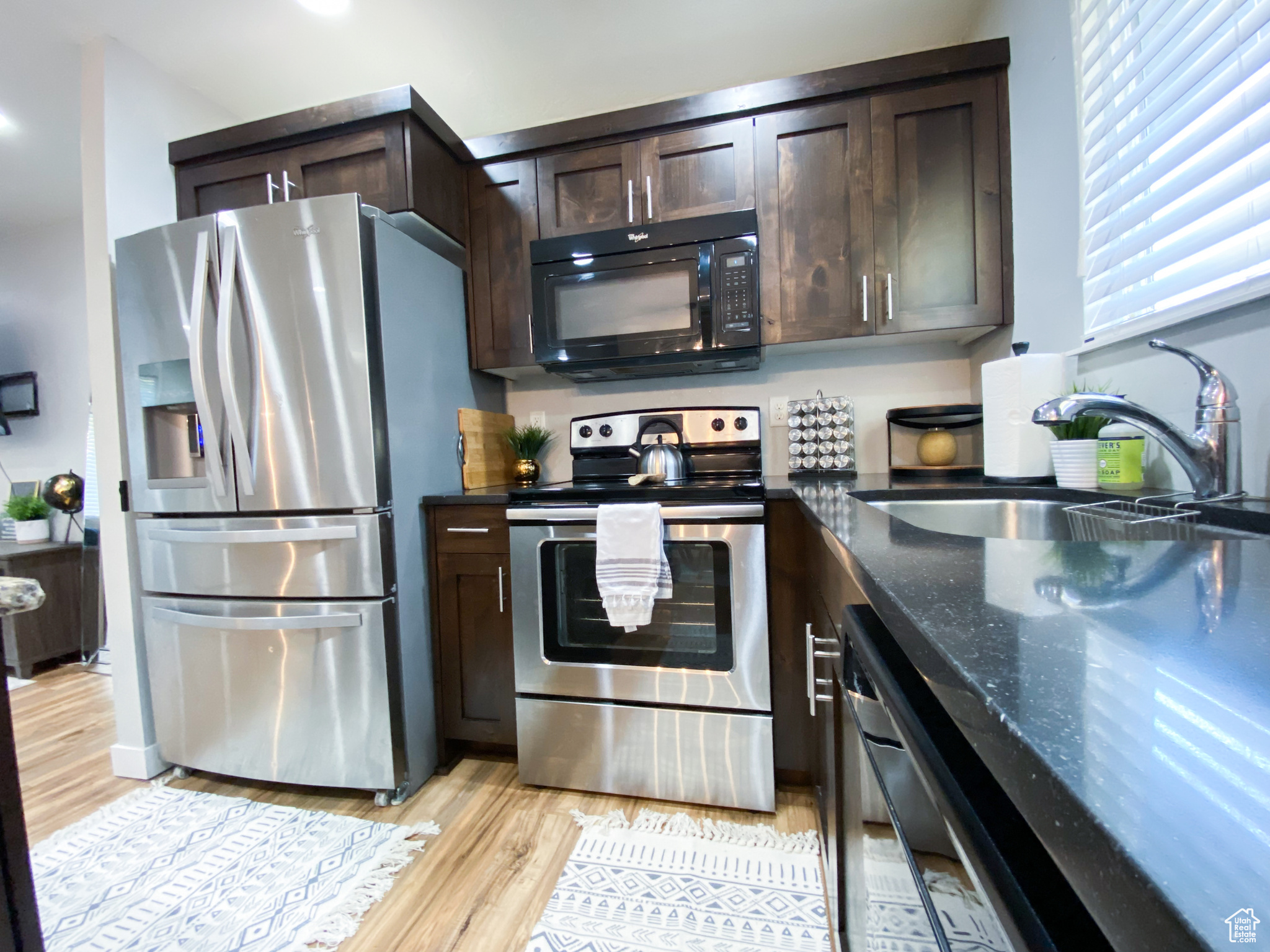 Upstairs Kitchen featuring dark stone counters, sink, light hardwood / wood-style floors, dark brown cabinetry, and stainless steel appliances