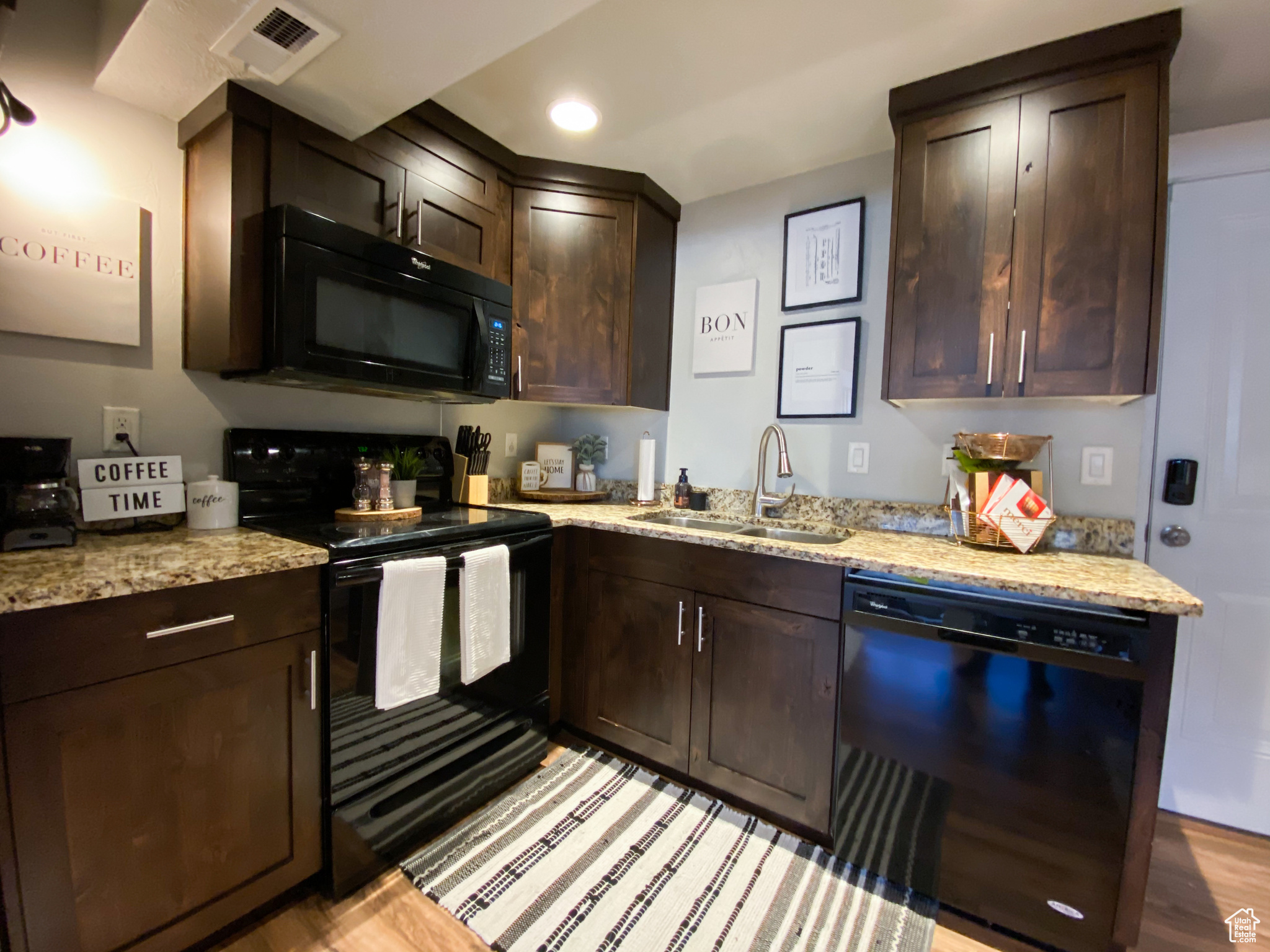 Downstairs Kitchen featuring dark brown cabinetry, sink, light stone counters, light hardwood / wood-style floors, and black/Stainless appliances