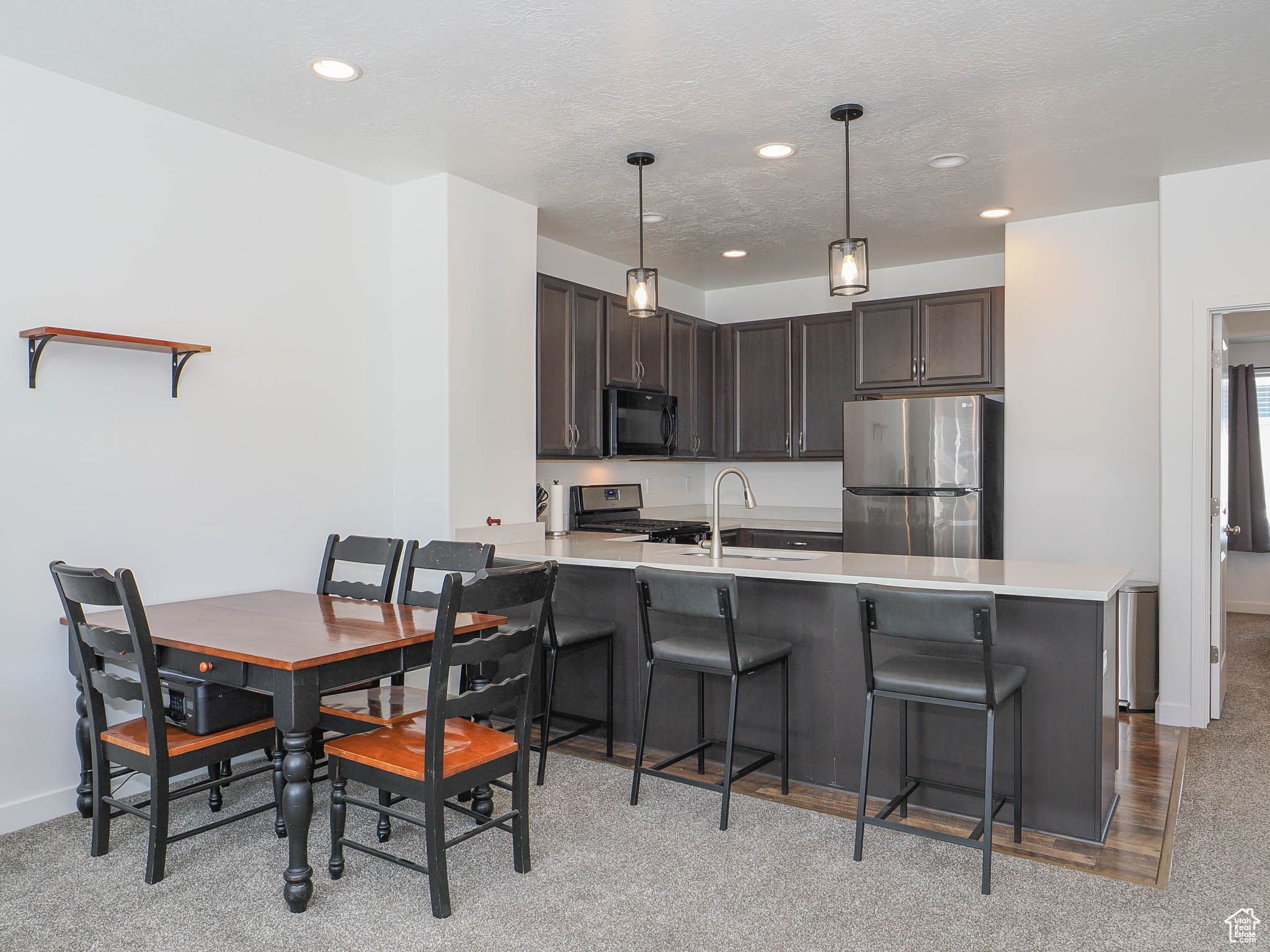 Kitchen with dark brown cabinetry, stainless steel appliances, kitchen peninsula, pendant lighting, and a breakfast bar area