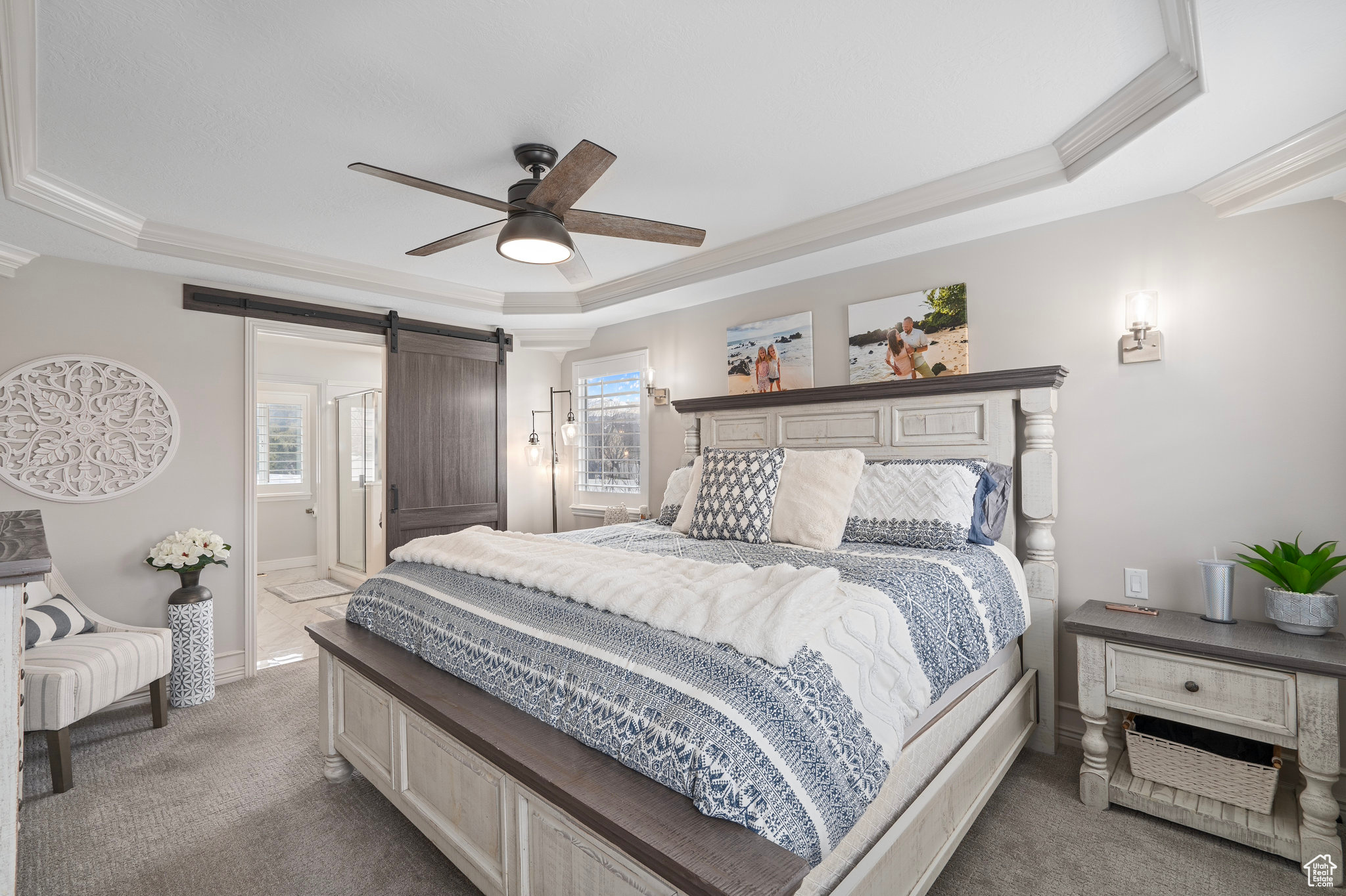 Carpeted bedroom featuring multiple windows, a barn door, a tray ceiling, and ceiling fan