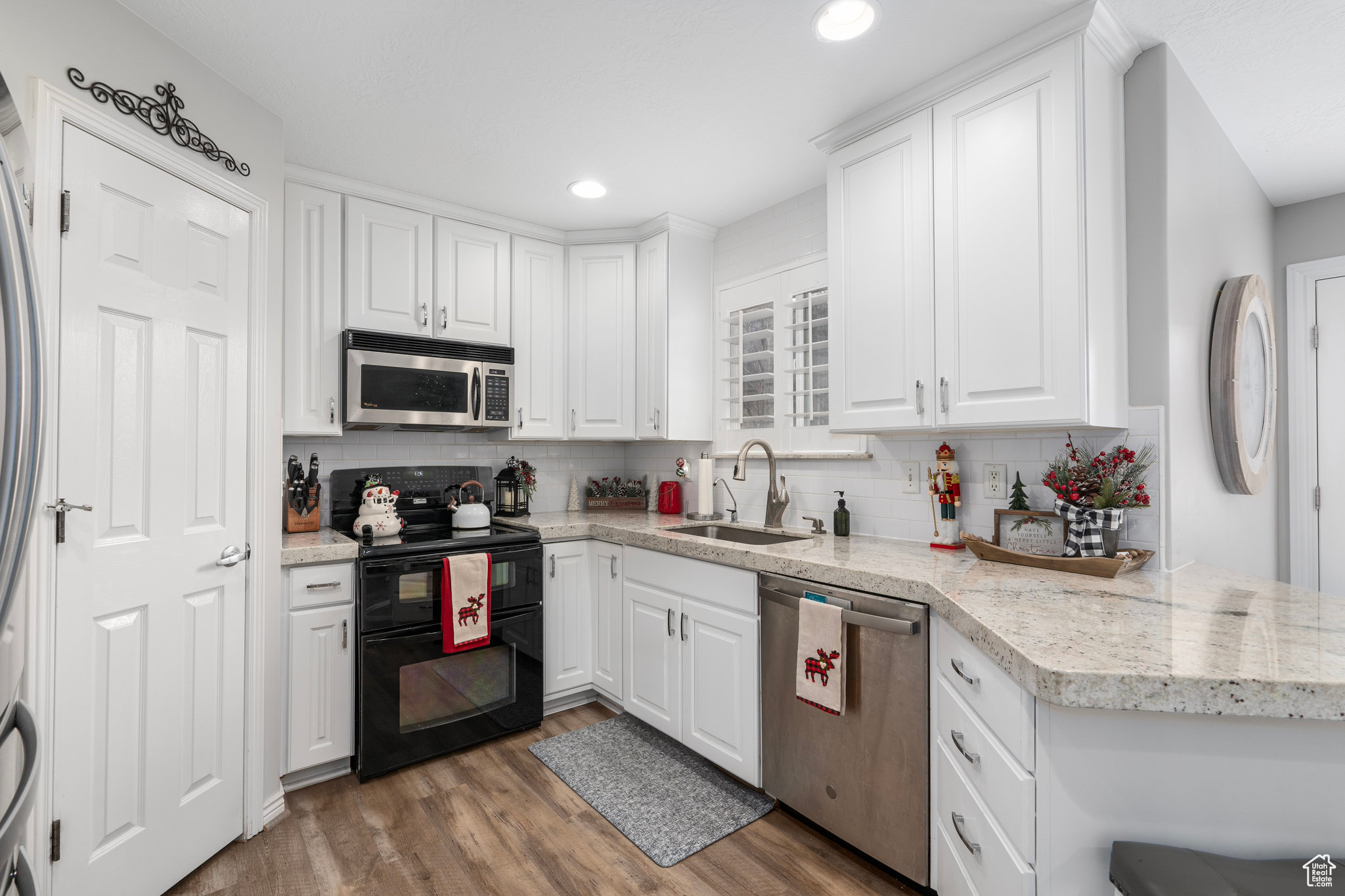 Kitchen with sink, stainless steel appliances, decorative backsplash, white cabinets, and hardwood / wood-style flooring