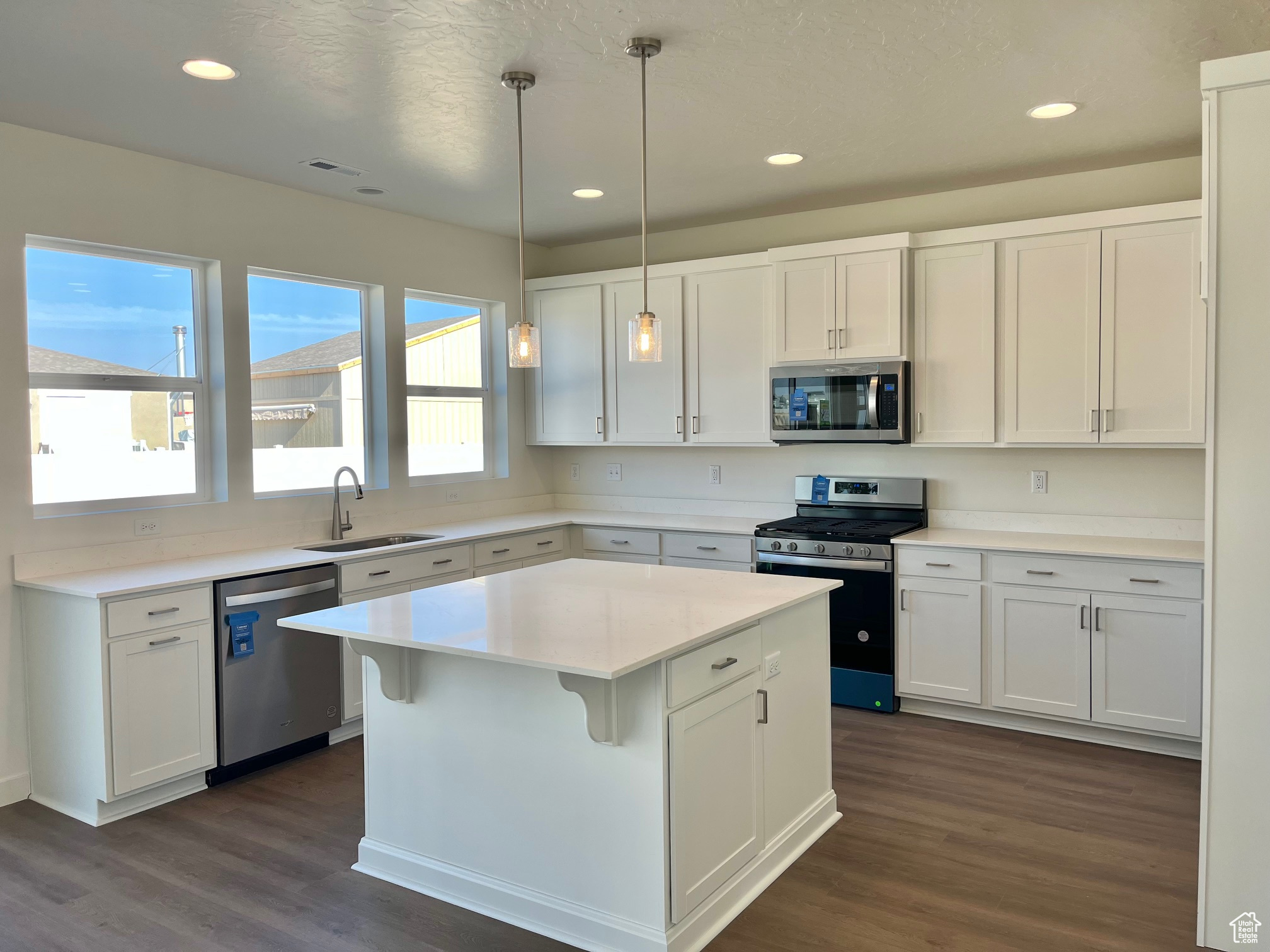 Kitchen with a center island, hanging light fixtures, sink, appliances with stainless steel finishes, and white cabinetry