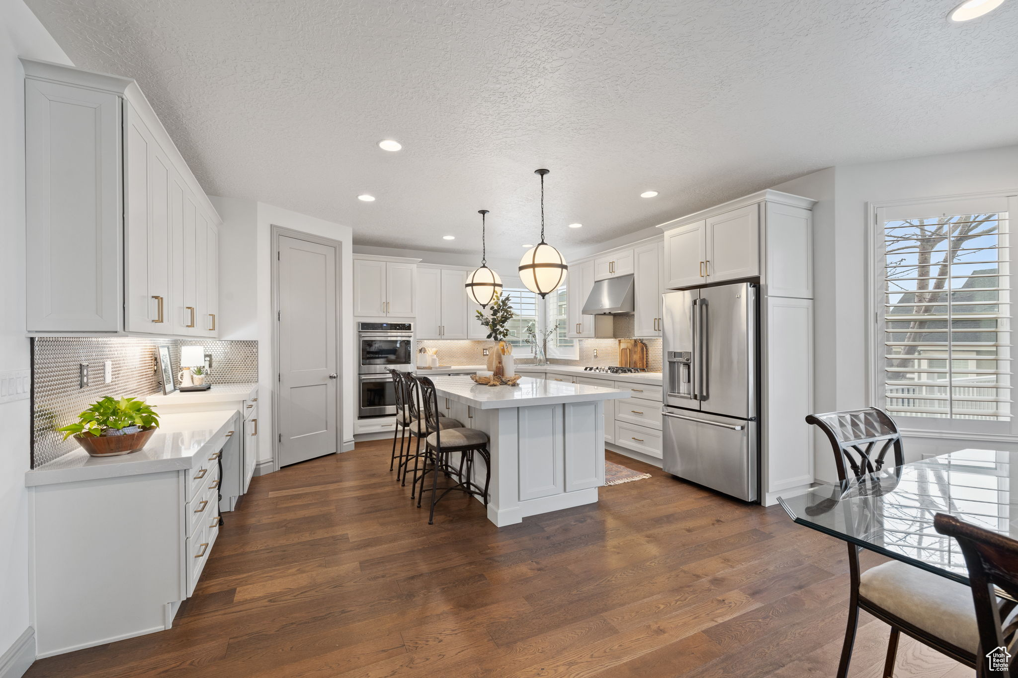 Kitchen with a center island, backsplash, white cabinets, appliances with stainless steel finishes, and decorative light fixtures