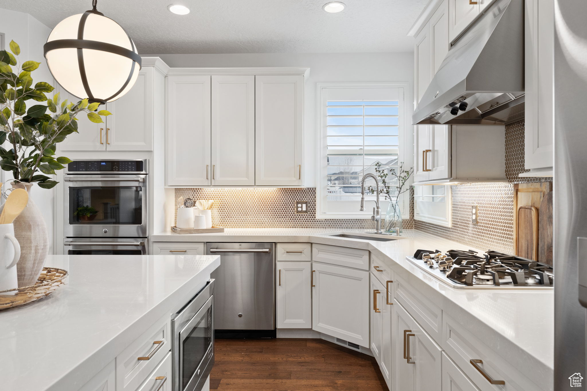 Kitchen featuring stainless steel appliances, pendant lighting, white cabinets, and exhaust hood