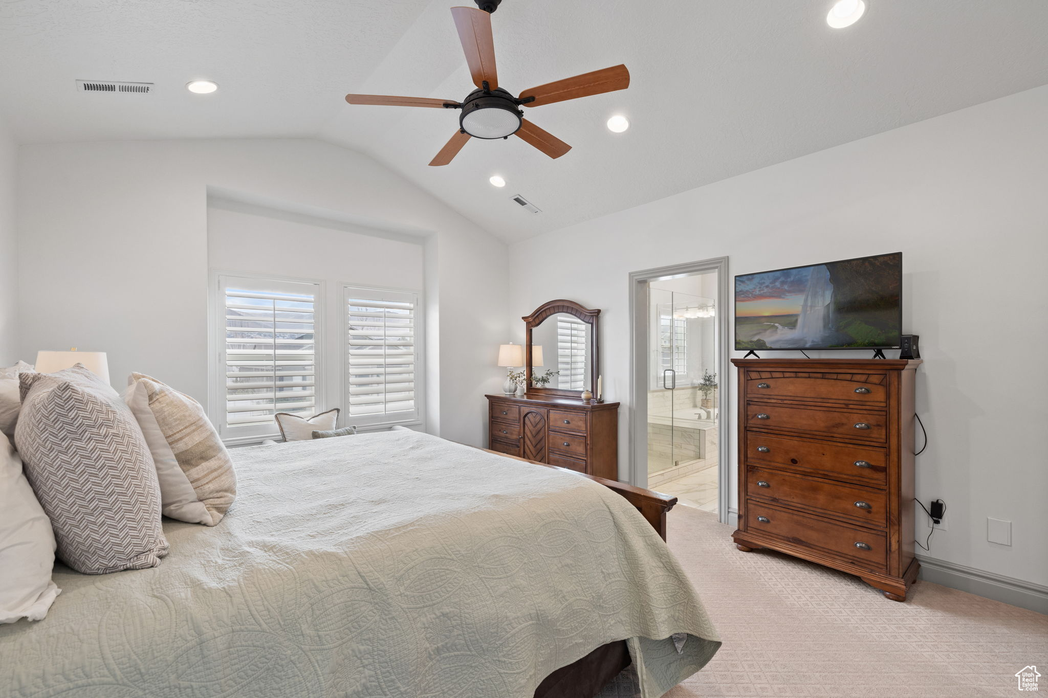 Carpeted bedroom with ensuite bathroom, ceiling fan, and vaulted ceiling