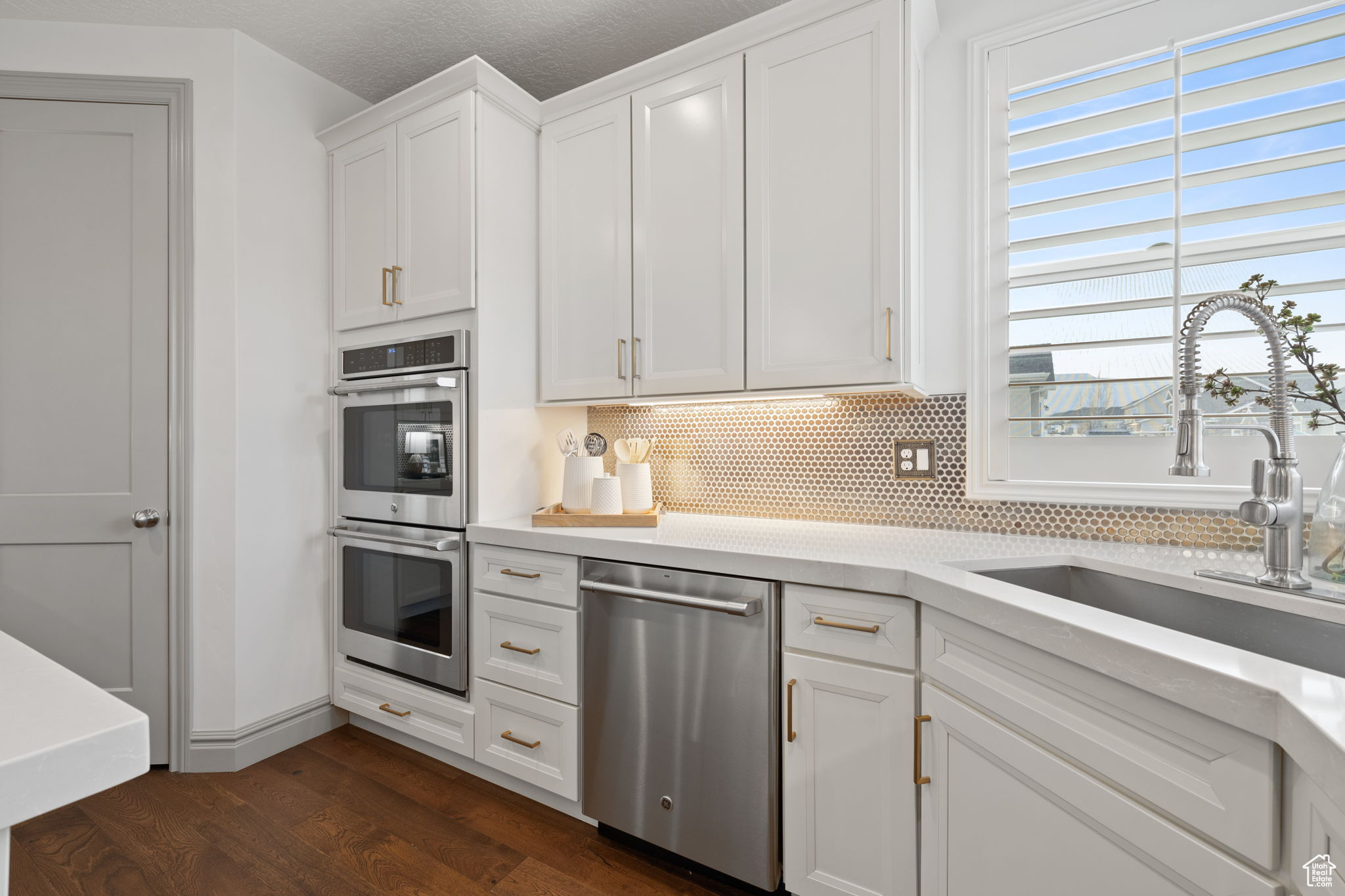 Kitchen featuring appliances with stainless steel finishes, tasteful backsplash, dark wood-type flooring, sink, and white cabinetry