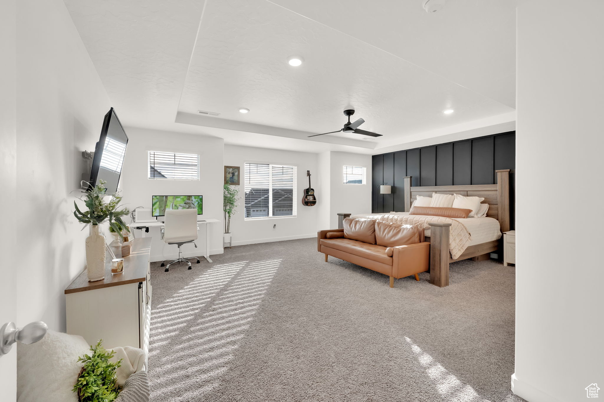 Bedroom with a raised ceiling, ceiling fan, and light carpet