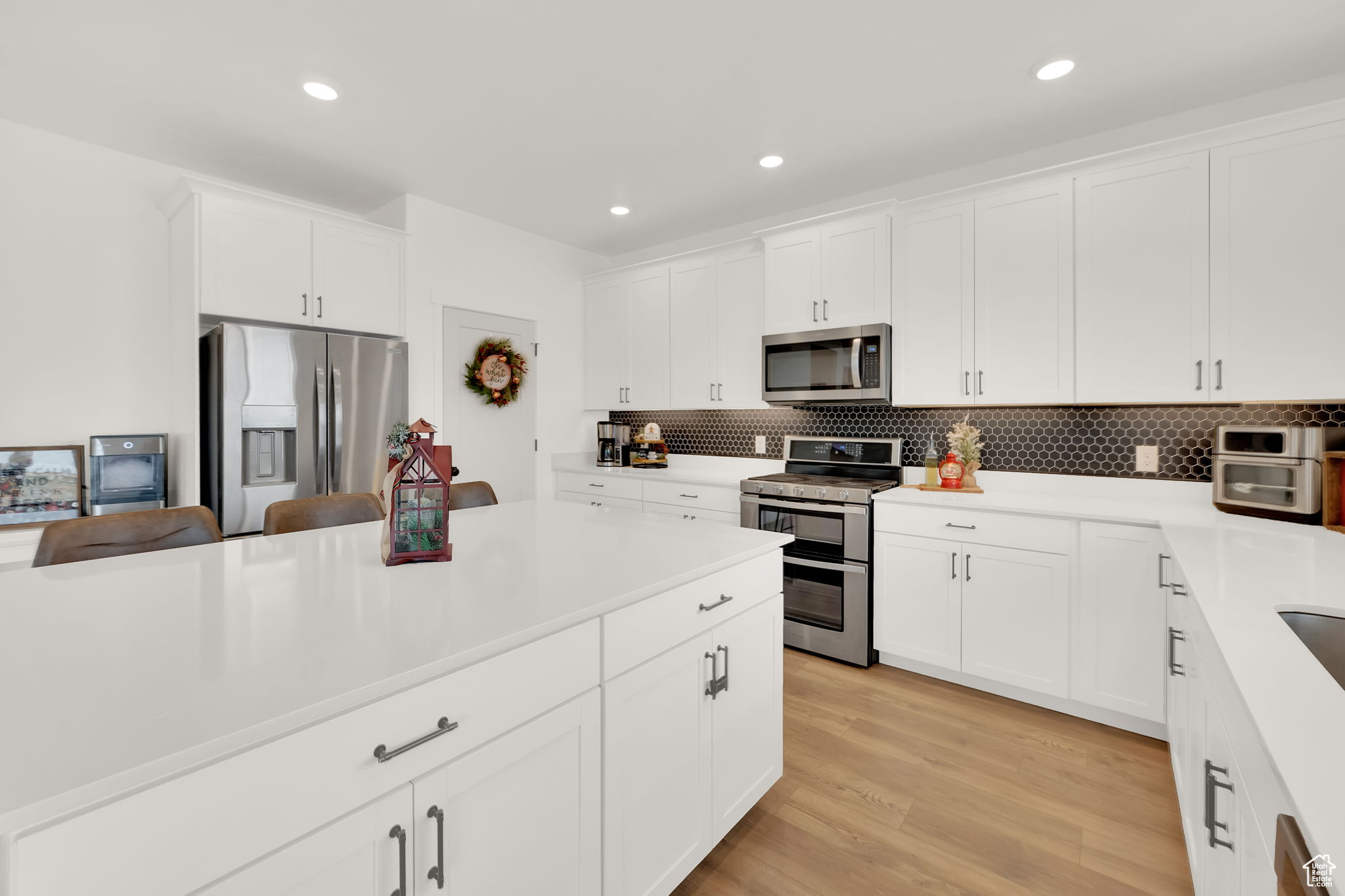 Kitchen featuring light wood-type flooring, white cabinetry, stainless steel appliances, and tasteful backsplash