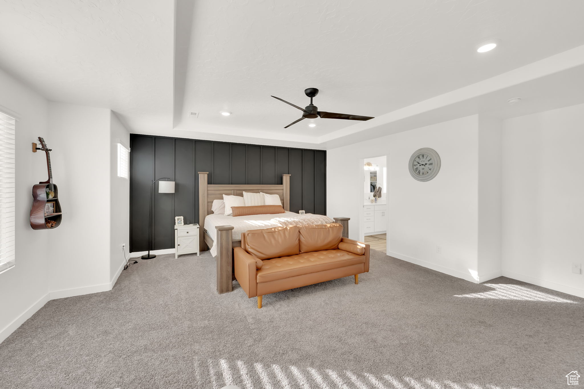 Bedroom featuring light carpet, a raised ceiling, ceiling fan, multiple windows, and connected bathroom