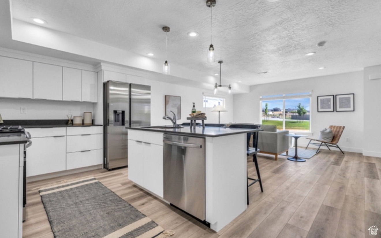 Kitchen with stainless steel appliances, a kitchen island with sink, sink, decorative light fixtures, and white cabinetry