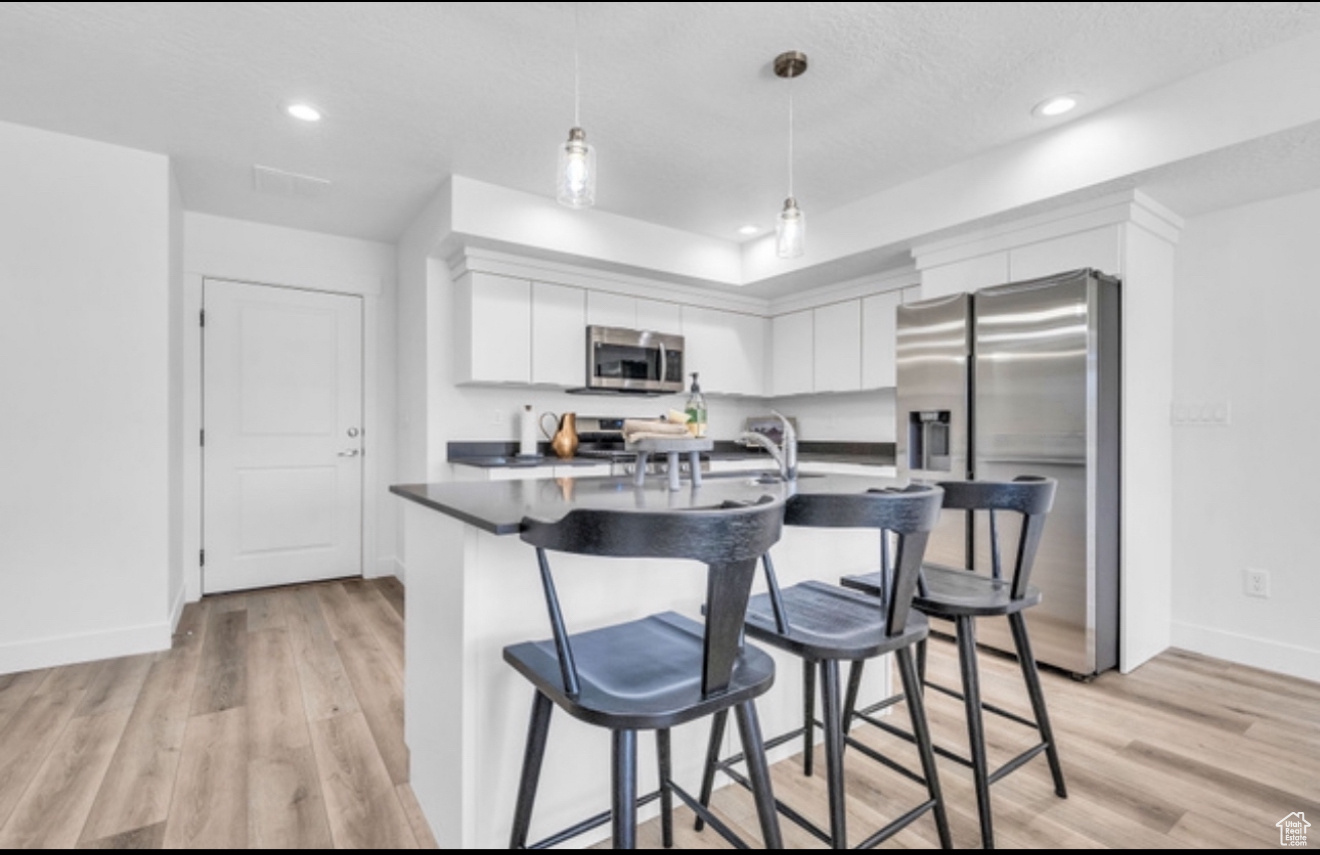 Kitchen with pendant lighting, white cabinets, light hardwood / wood-style flooring, appliances with stainless steel finishes, and a kitchen bar