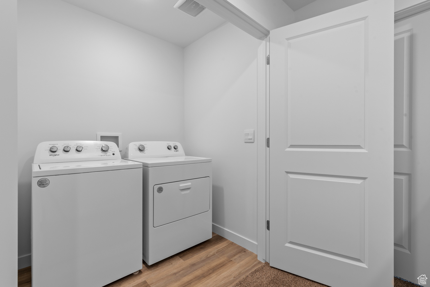 Clothes washing area with washer and clothes dryer and light hardwood / wood-style flooring