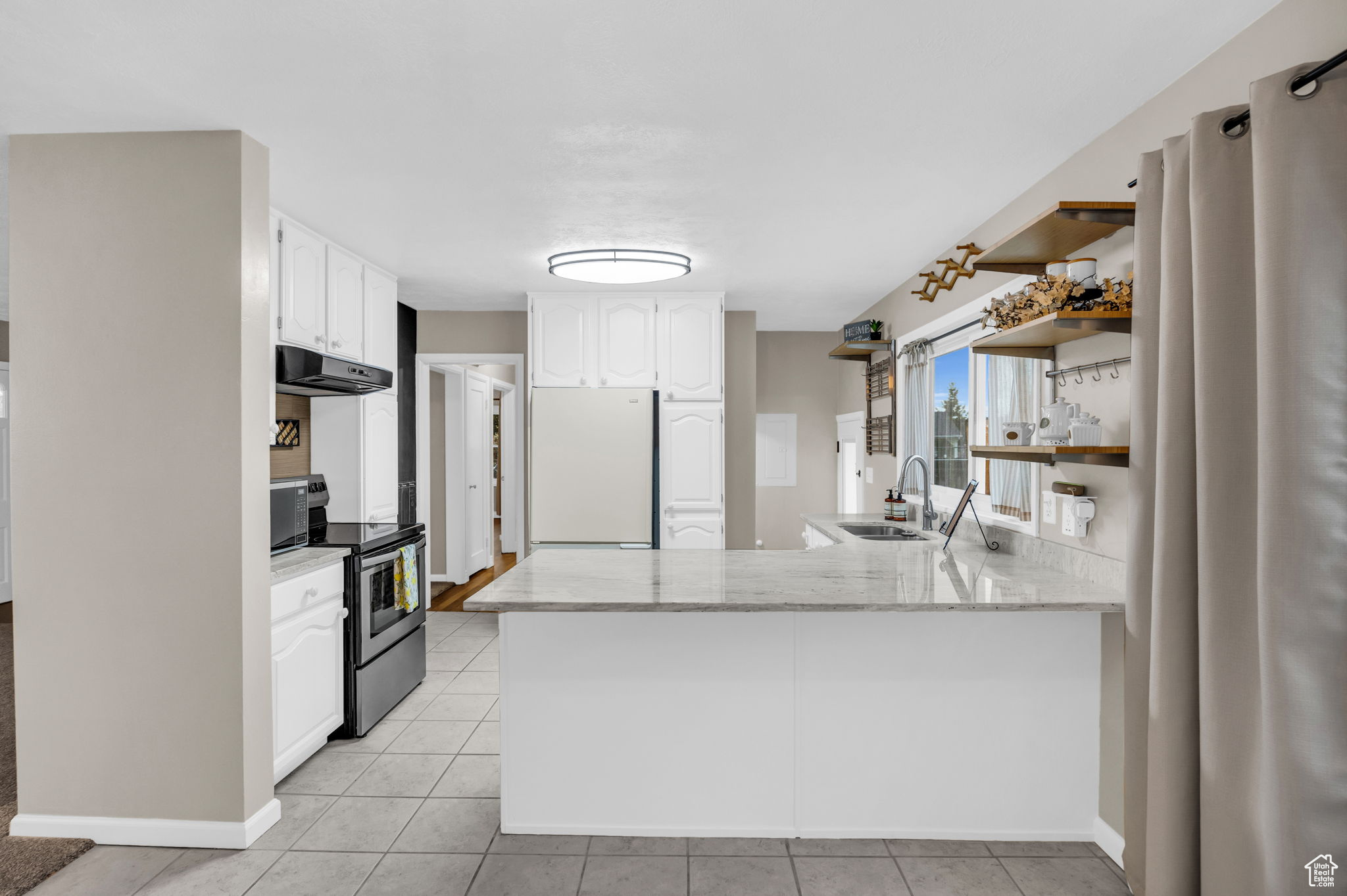 Kitchen featuring stainless steel range with electric cooktop,  refrigerator, sink, white cabinetry, and kitchen peninsula