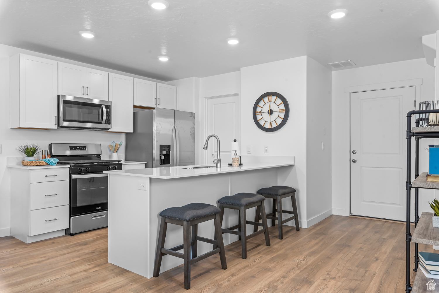 Kitchen featuring a kitchen breakfast bar, kitchen peninsula, sink, appliances with stainless steel finishes, and white cabinetry