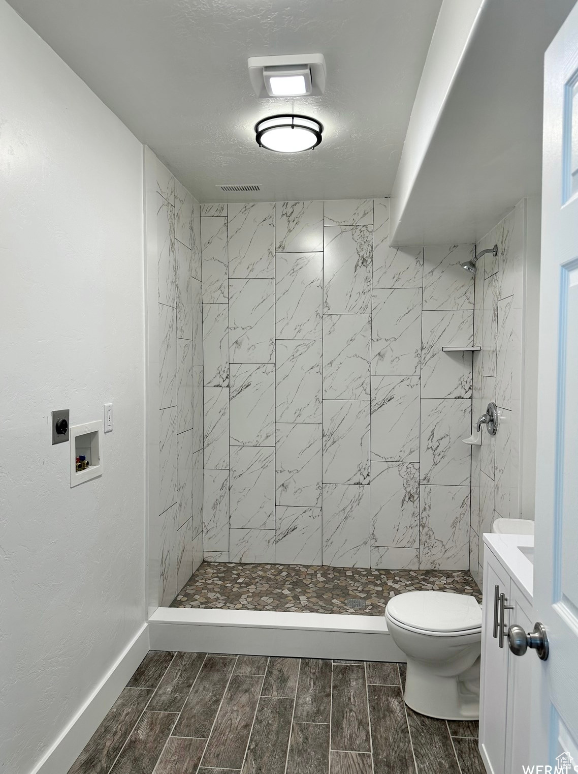 Bathroom featuring tiled shower, vanity, and toilet