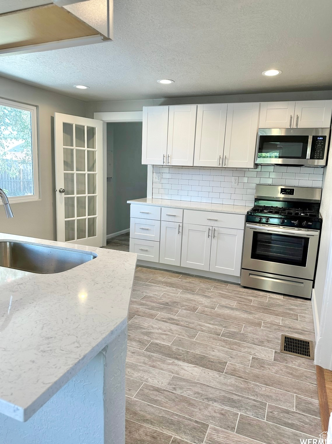 Kitchen featuring white cabinetry, sink, light stone countertops, and appliances with stainless steel finishes