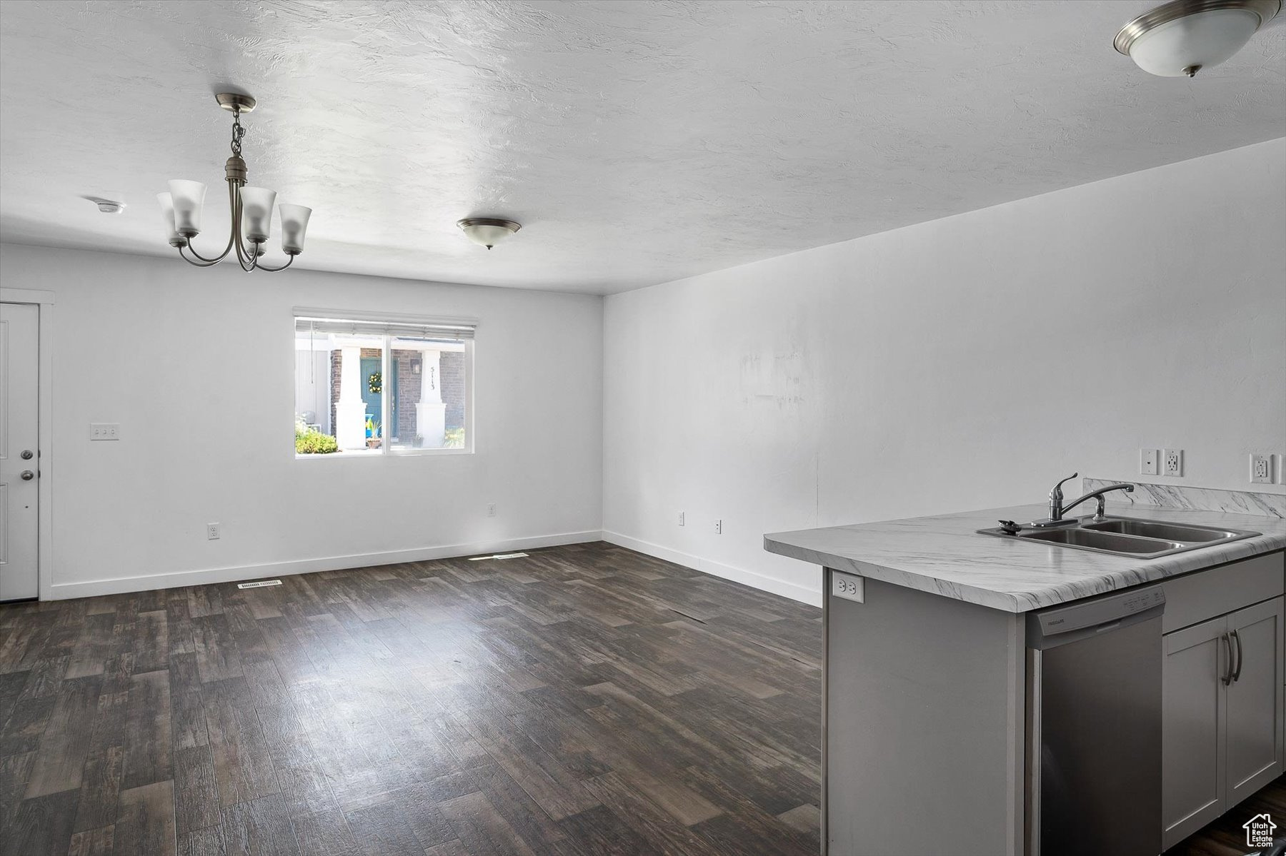 Interior space with gray cabinetry, an inviting chandelier, sink, stainless steel dishwasher, and decorative light fixtures