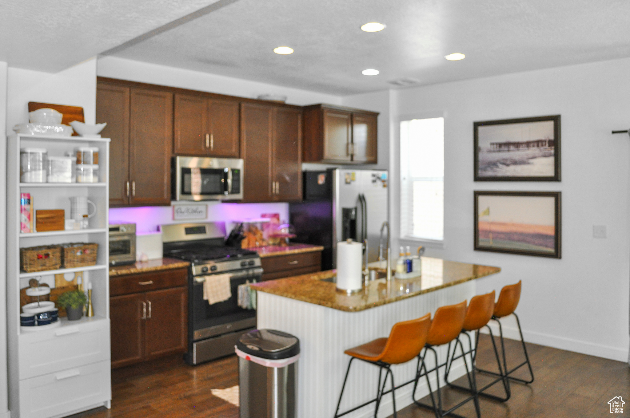 Kitchen with a kitchen bar, light stone counters, stainless steel appliances, dark hardwood / wood-style floors, and an island with sink