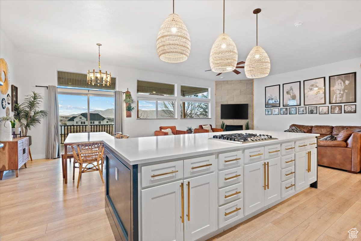 Kitchen featuring stainless steel gas cooktop, white cabinets, light hardwood / wood-style floors, pendant lighting, and a kitchen island