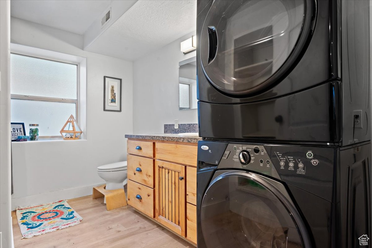 Washroom with stacked washing maching and dryer, a textured ceiling, and light hardwood / wood-style flooring