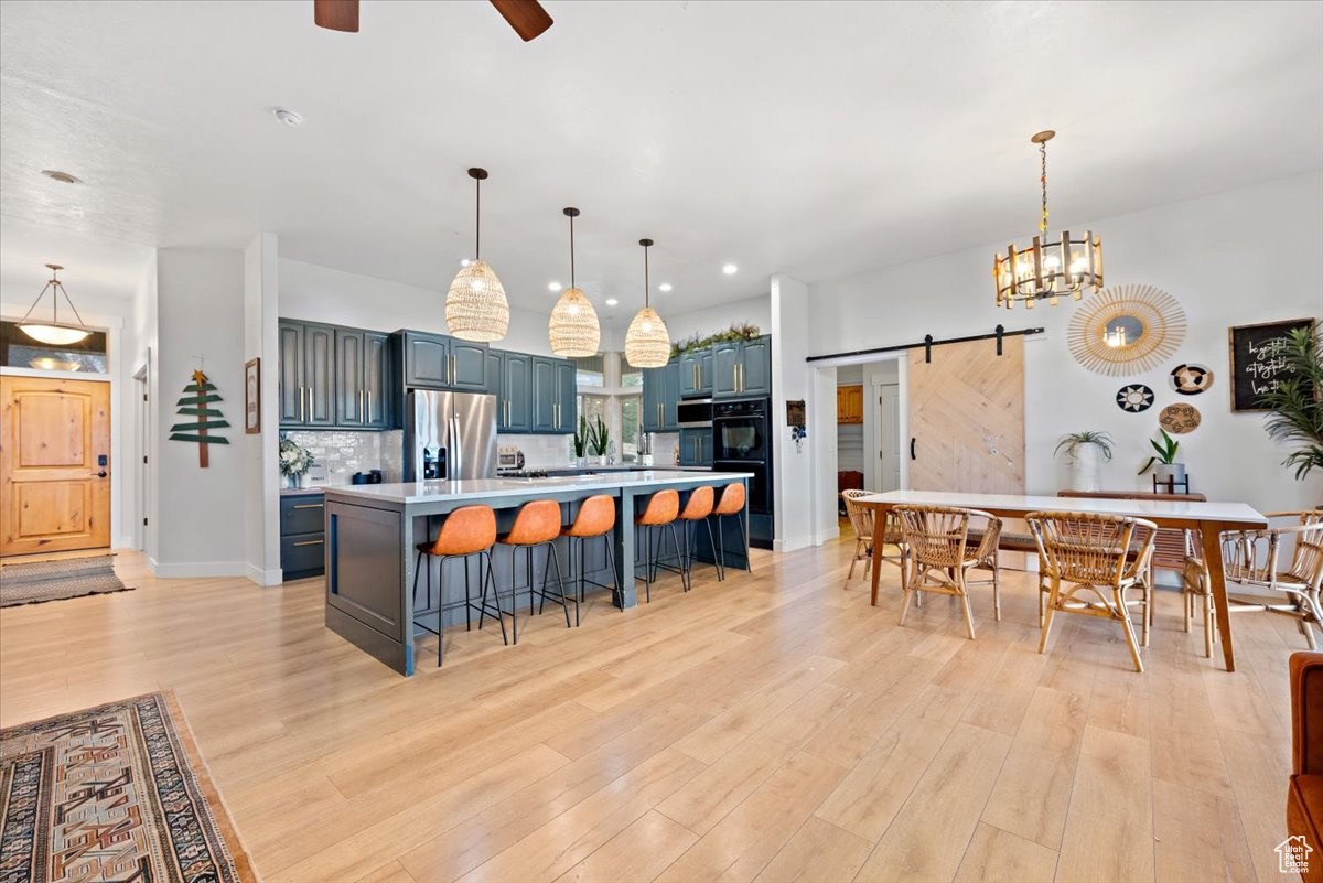 Kitchen with a center island, a barn door, stainless steel fridge with ice dispenser, light hardwood / wood-style flooring, and decorative light fixtures