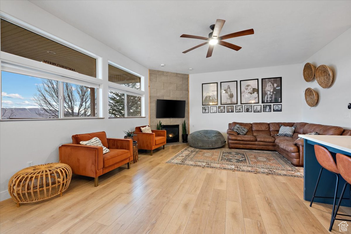 Living room with ceiling fan, a healthy amount of sunlight, light wood-type flooring, and a tiled fireplace