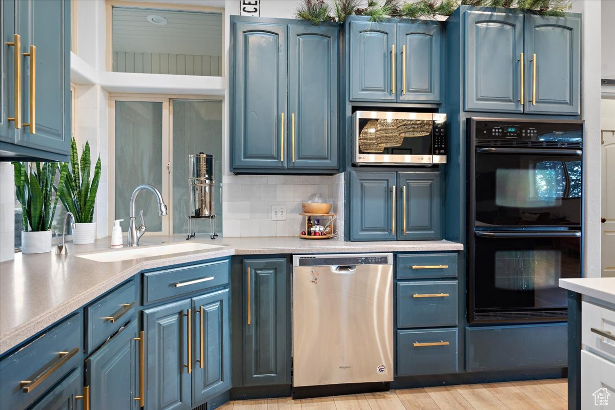 Kitchen featuring decorative backsplash, sink, blue cabinetry, and appliances with stainless steel finishes